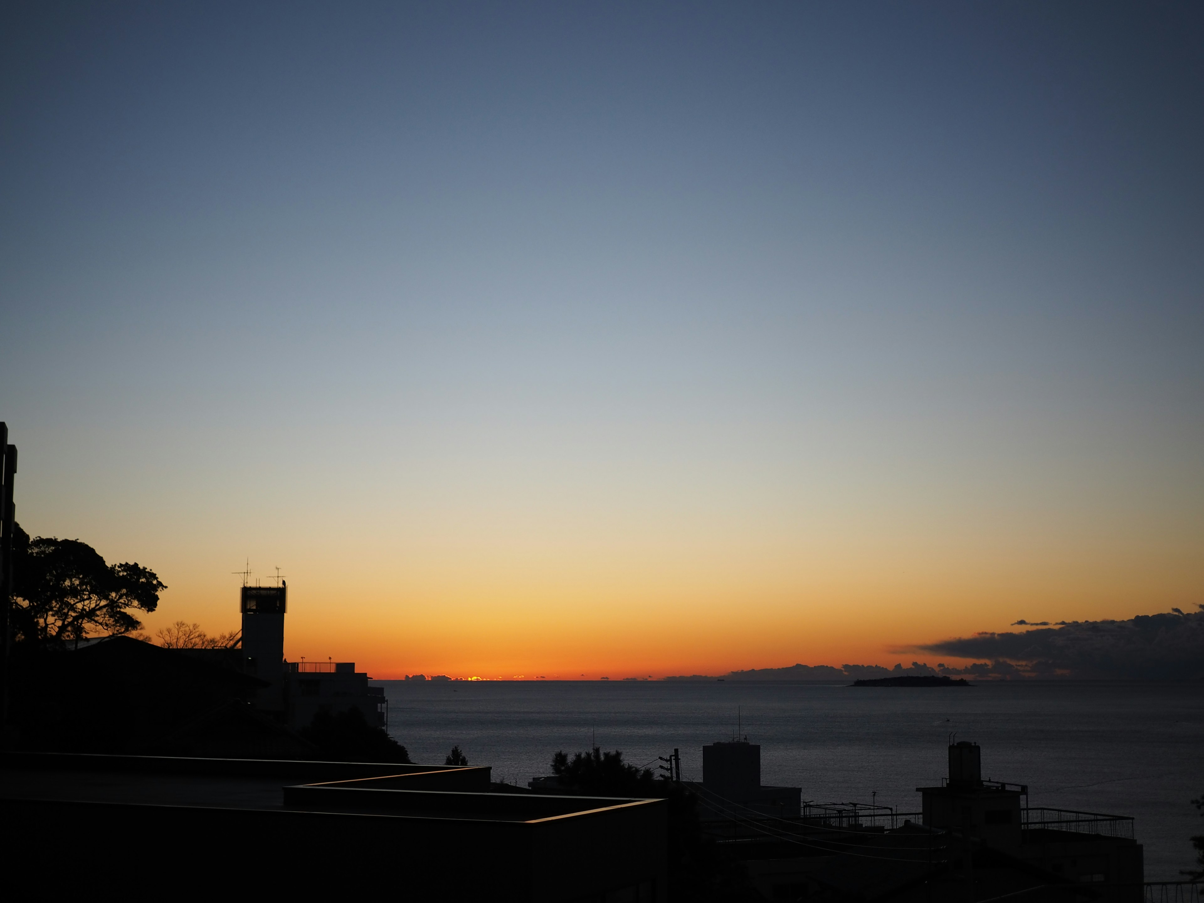 Silhouette von Gebäuden vor einem Sonnenuntergang über dem Meer