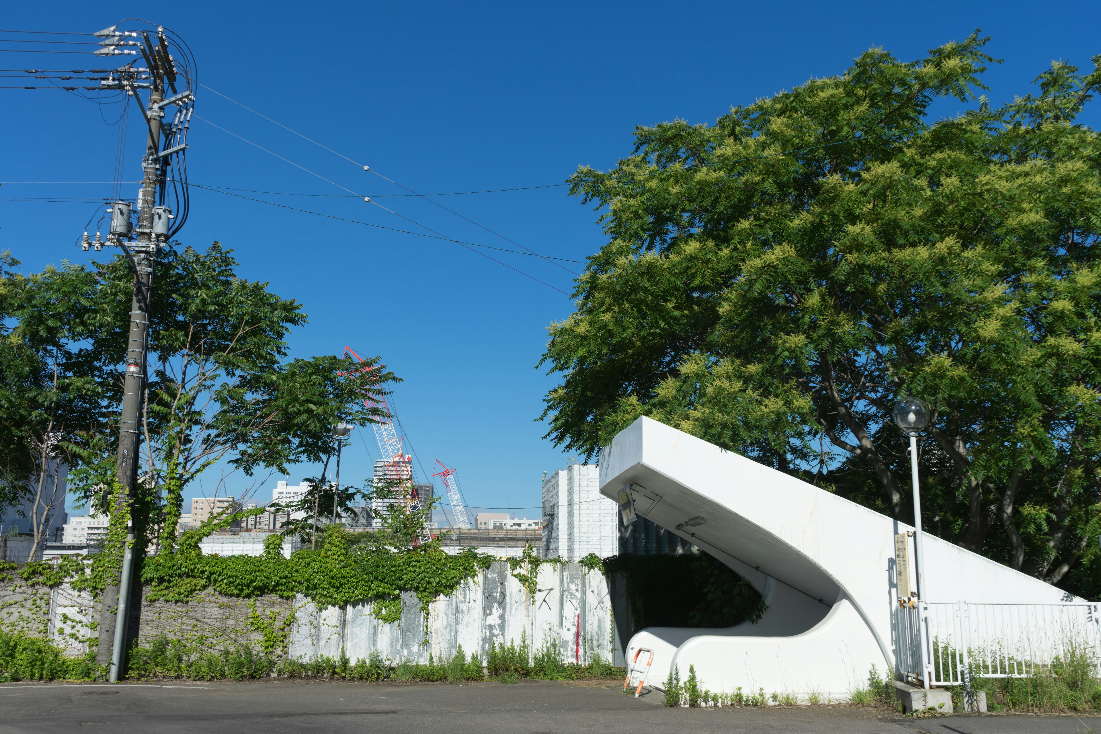 A modern white architectural structure under a clear blue sky surrounded by green trees