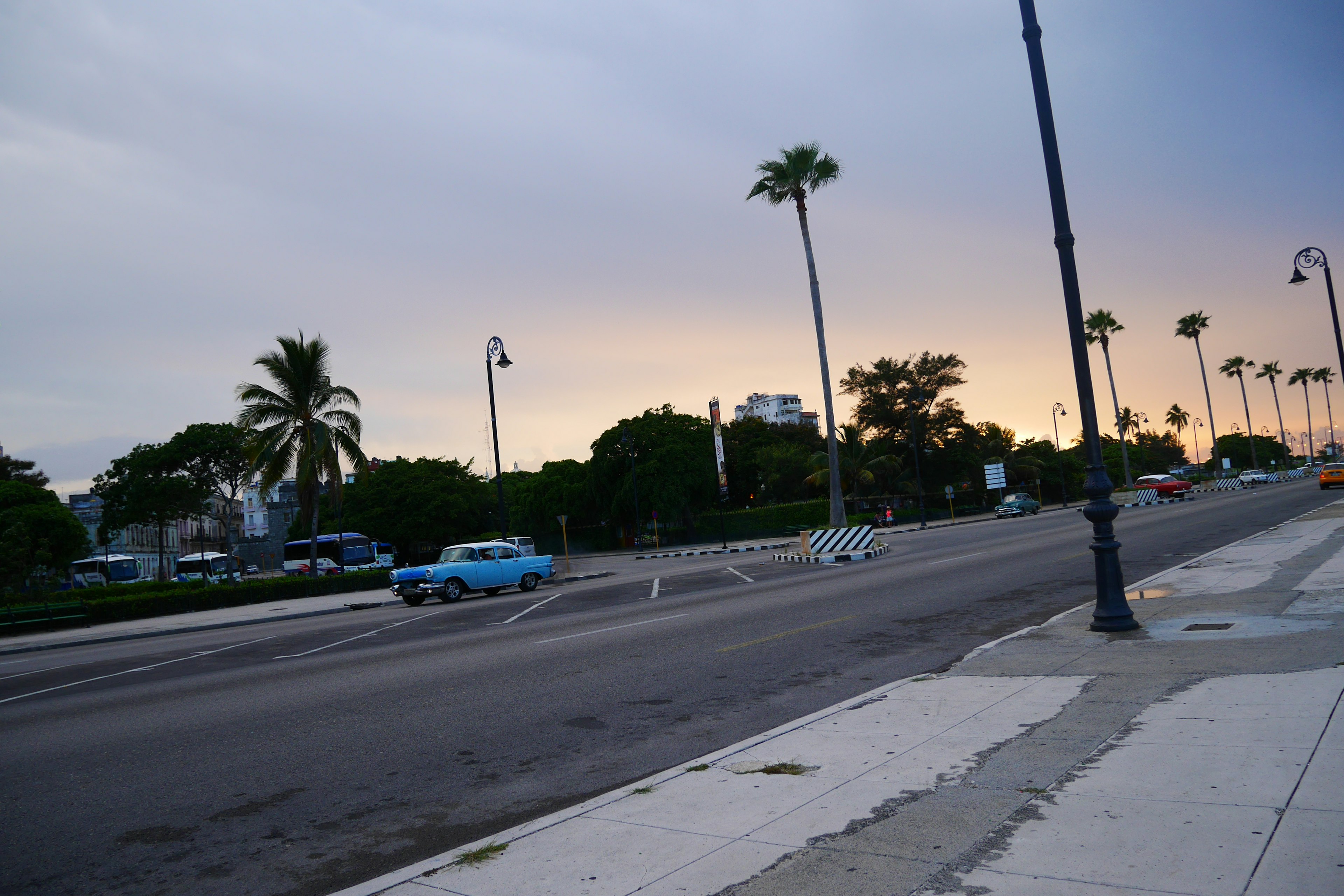 Une route bordée de palmiers et d'une voiture classique bleue au crépuscule