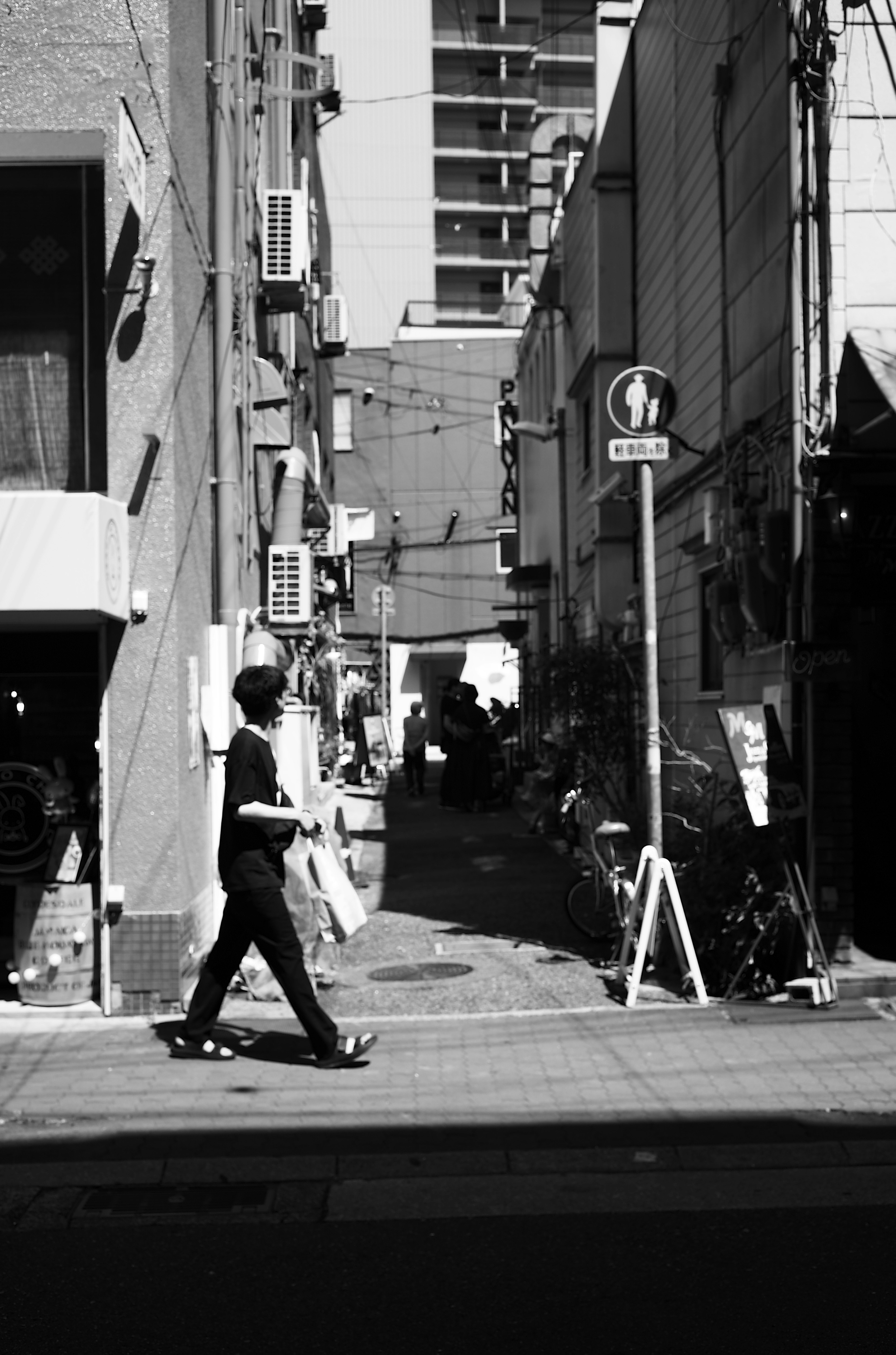 A person walking on a black and white street corner with a narrow alley