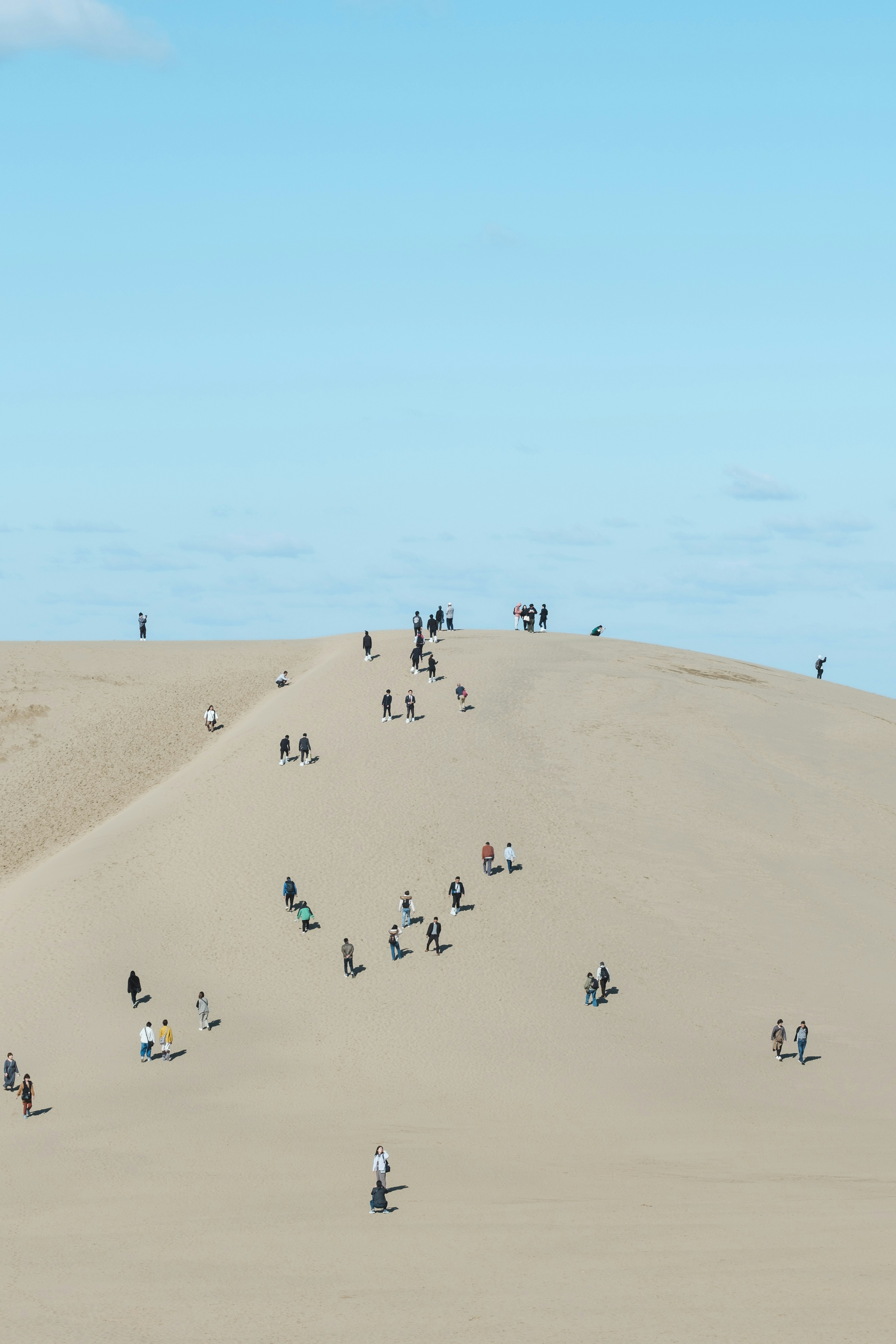 People climbing a sand dune under a blue sky