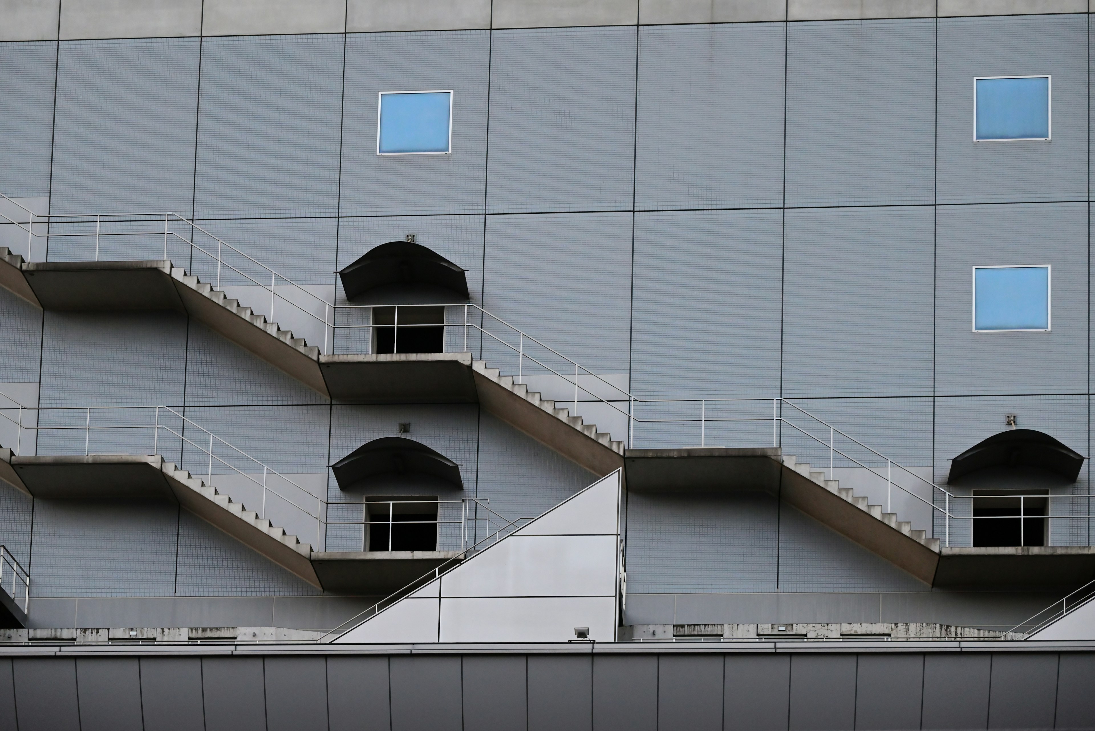 Vista lateral de un edificio con paredes grises que presenta escaleras y ventanas