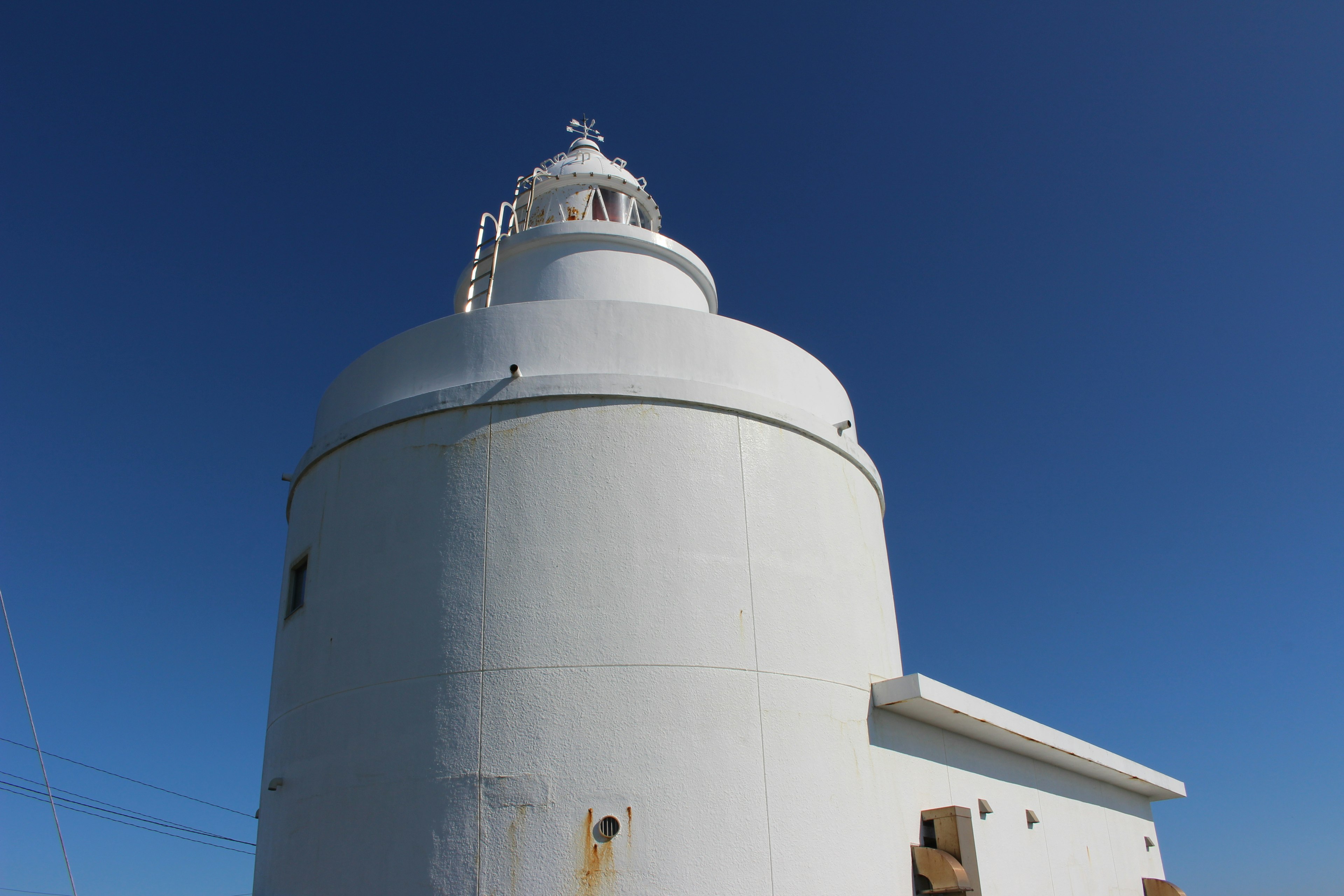 Side view of a white lighthouse under a blue sky