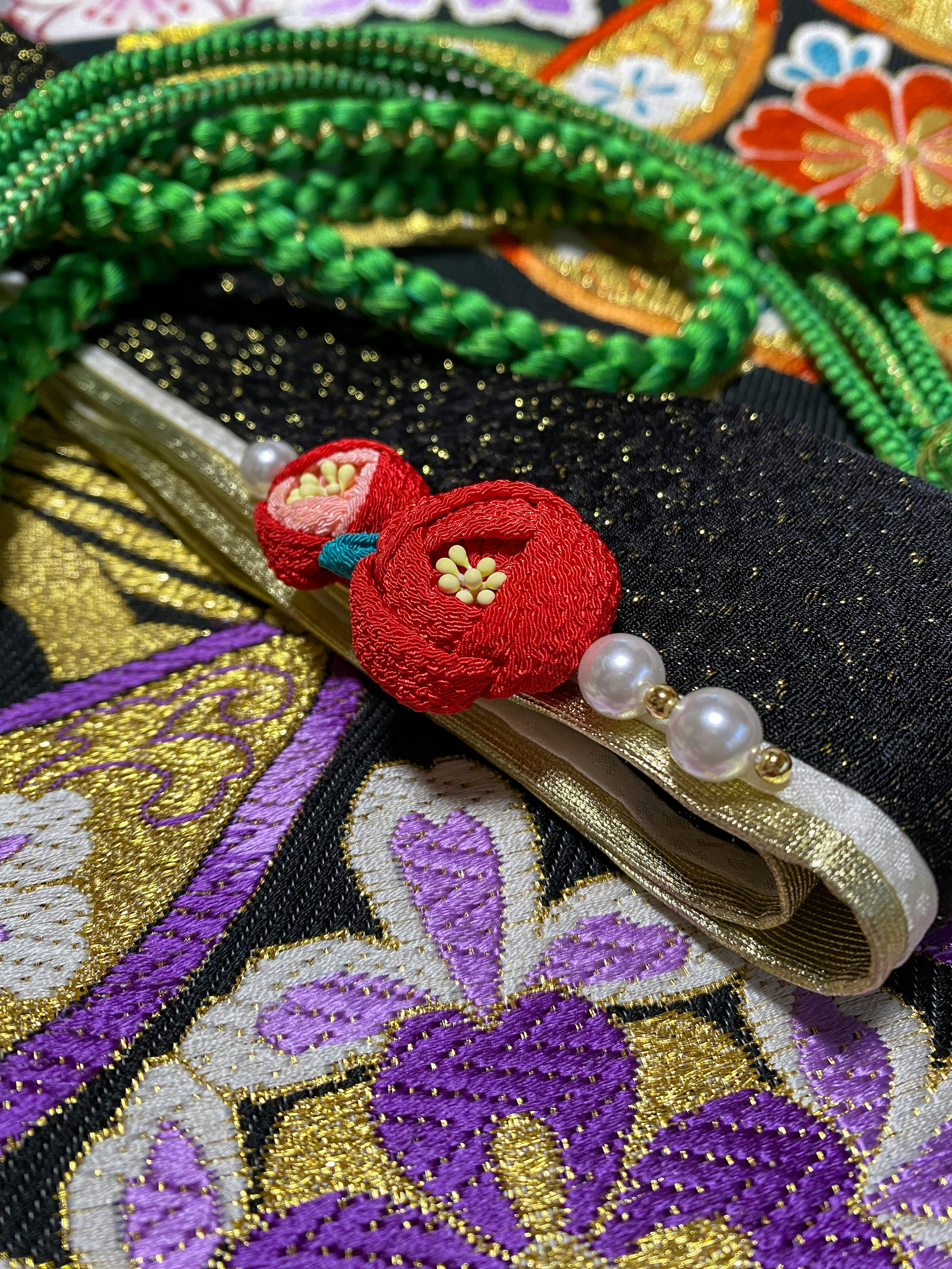 A decorative obi featuring red flower embellishments and pearls on a colorful kimono background