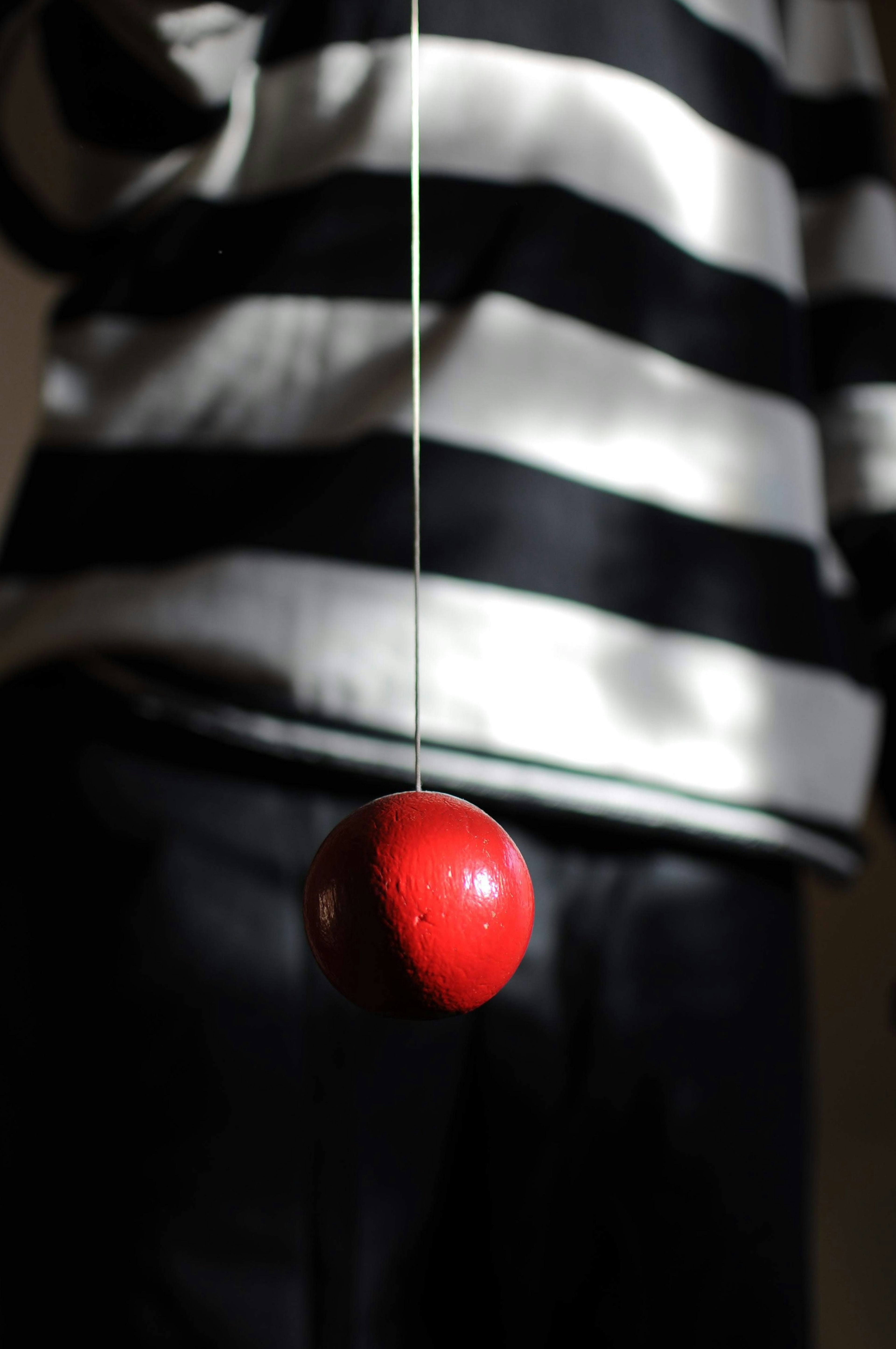 A red ball hanging from a string held by a person in a striped sweater