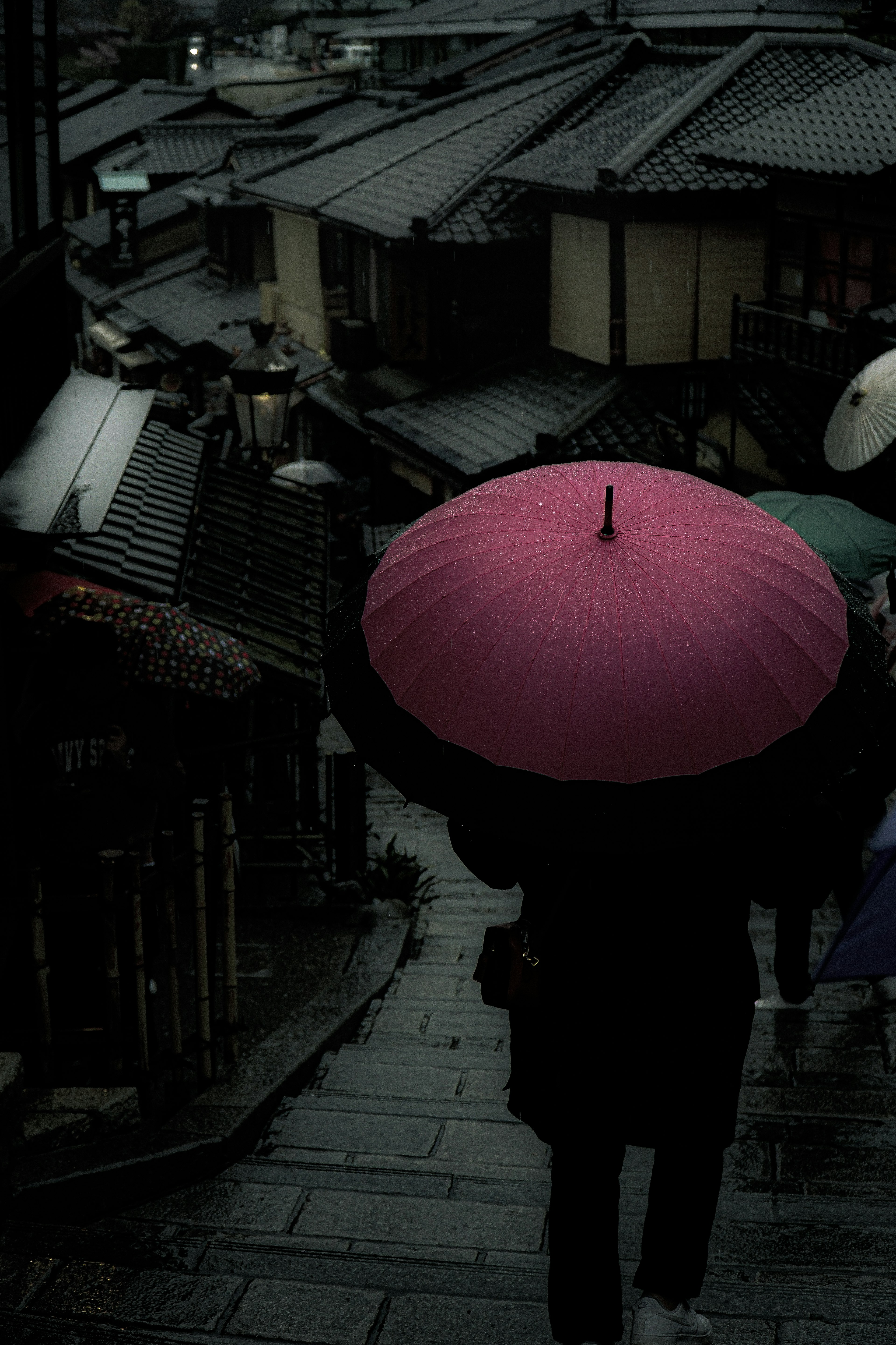 雨の中、ピンクの傘を持った人が古い町並みを歩いている風景