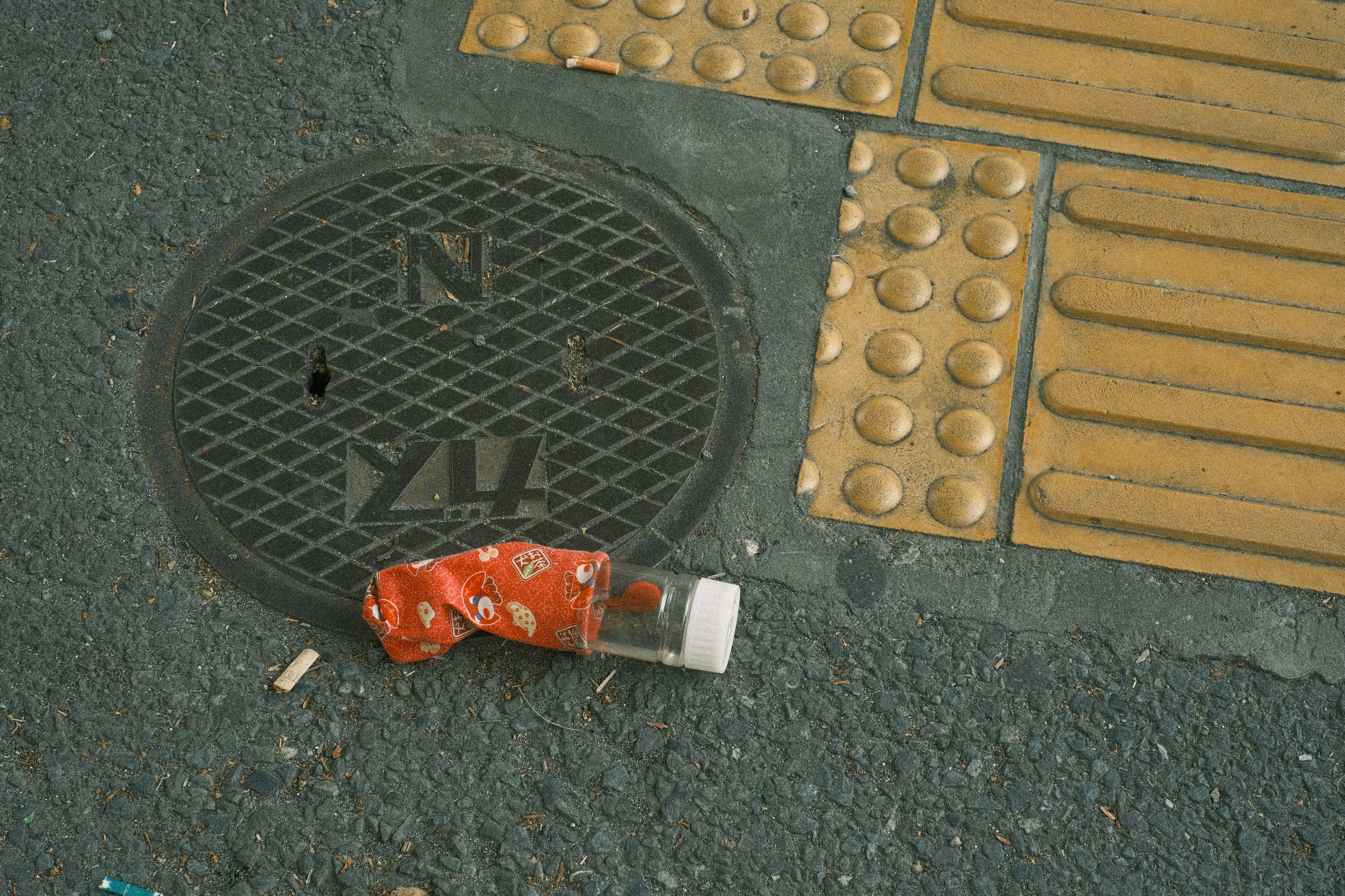 Red packaging on the ground next to a manhole cover