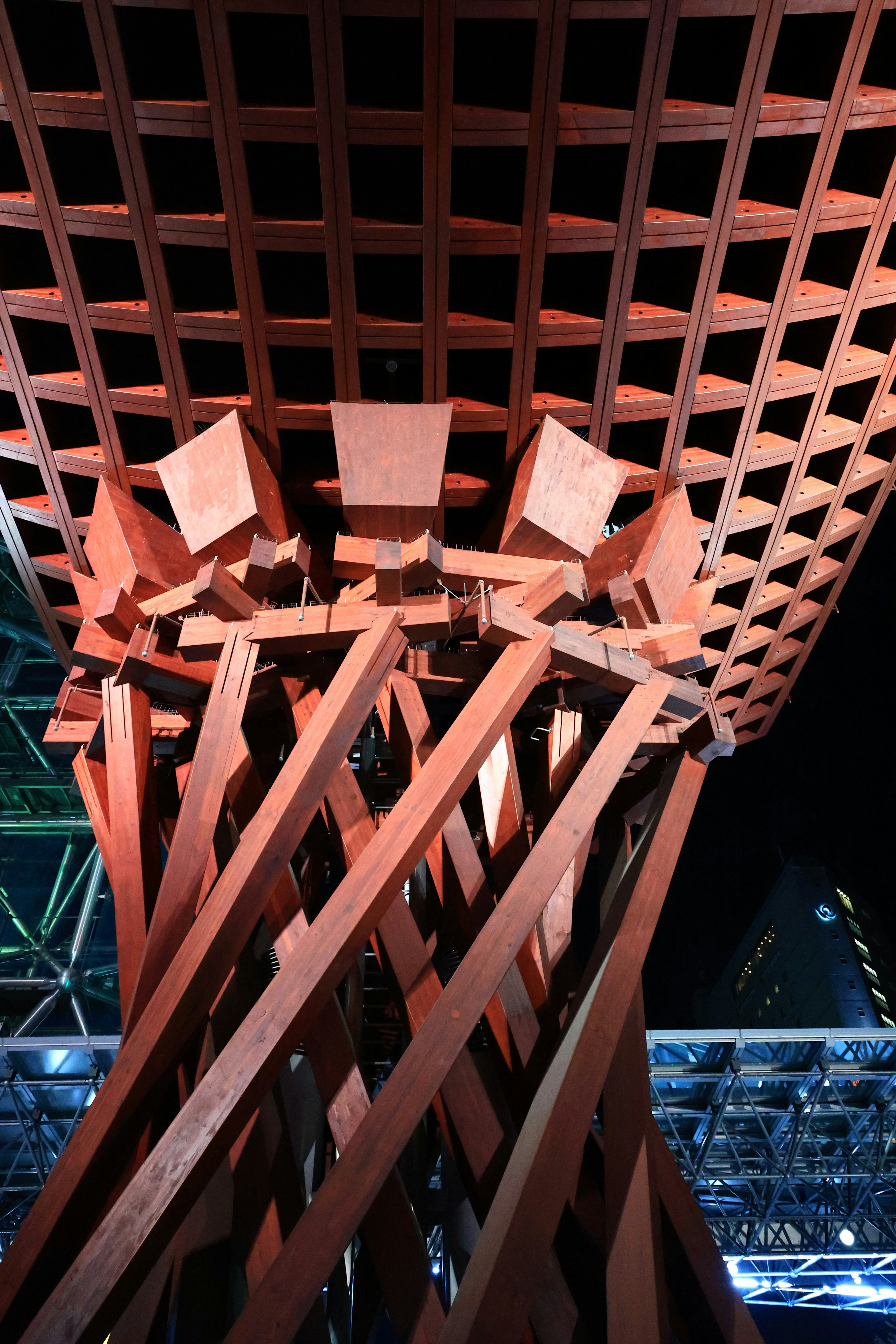 View from below a wooden structure at night showcasing intersecting wood beams and a lattice design