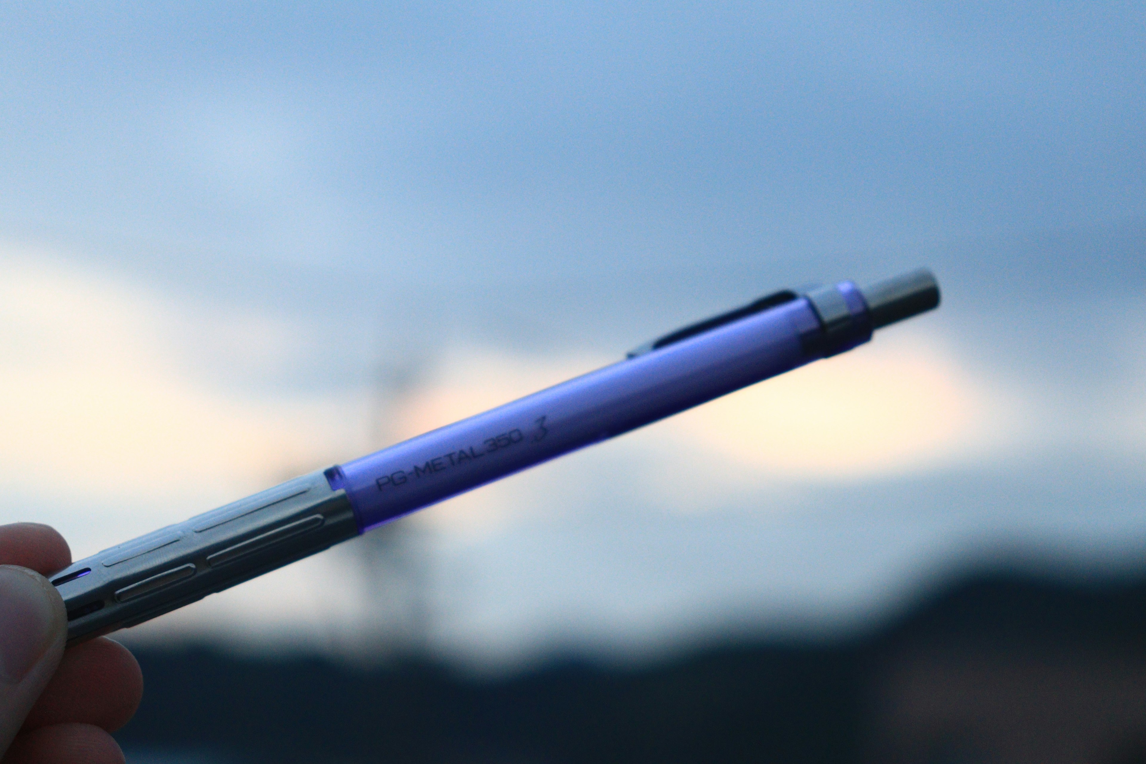 Hand holding a purple pen against a blurred sky background