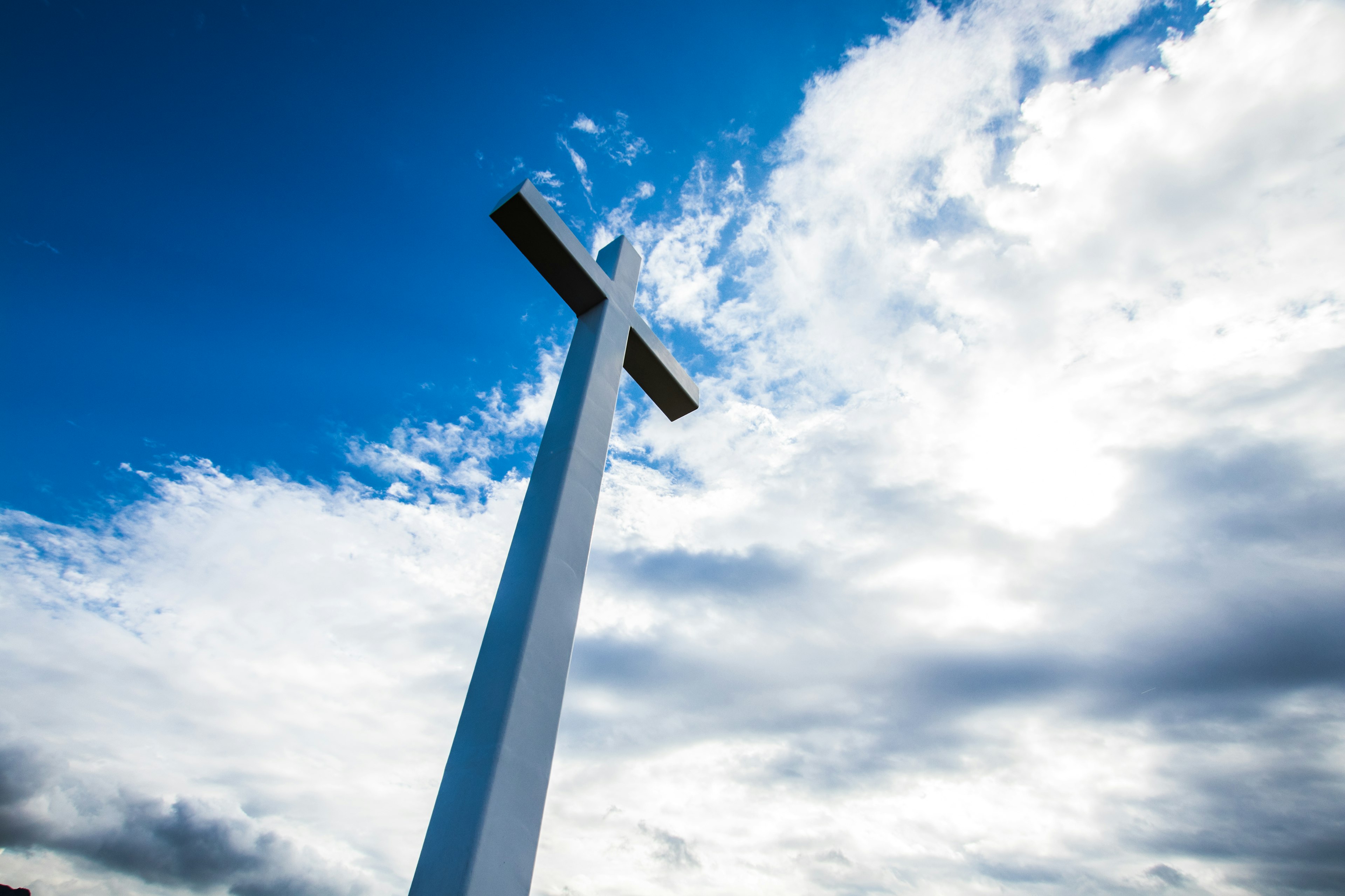 A white cross standing under a blue sky with clouds