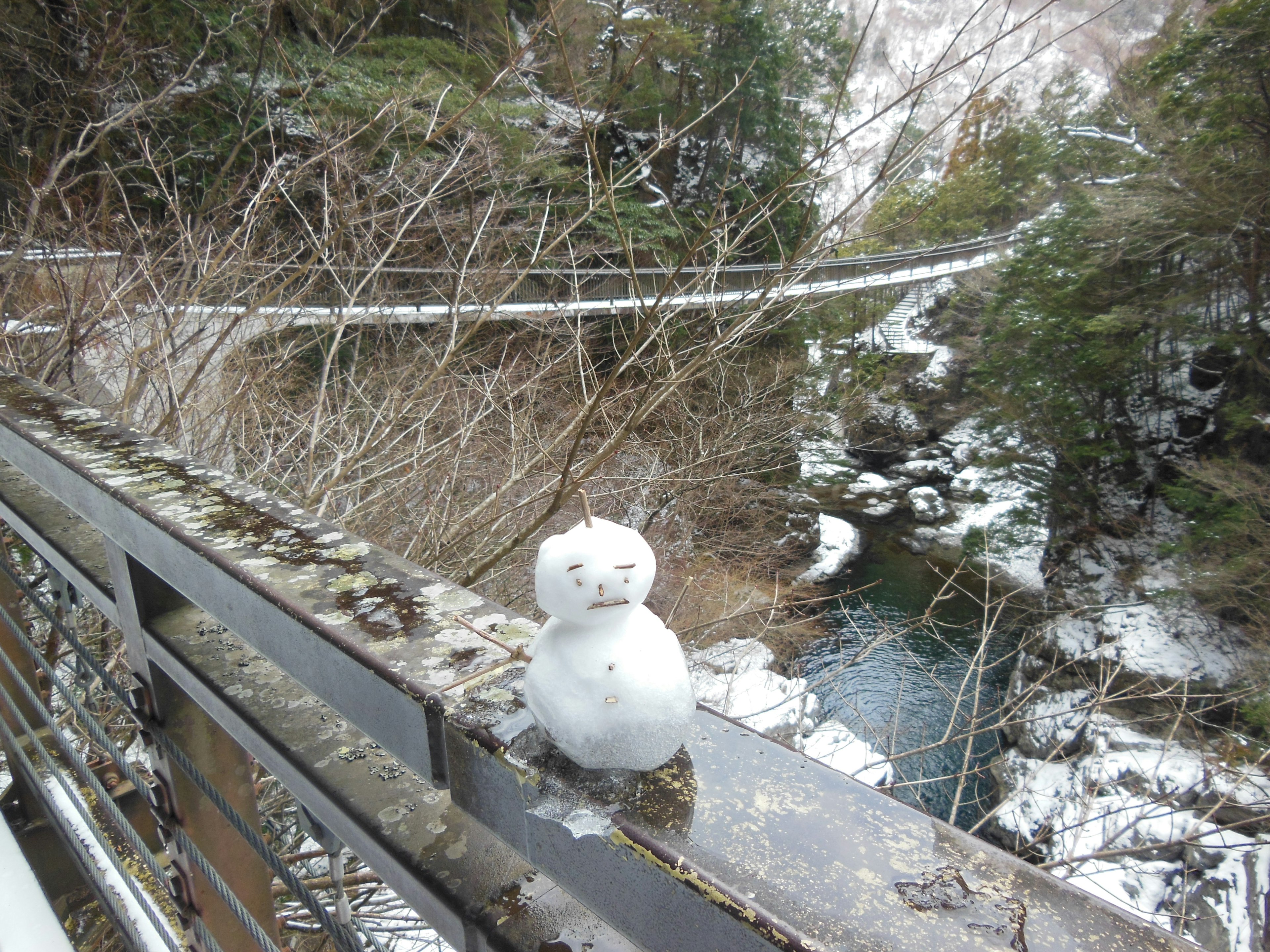 Un bonhomme de neige posé sur la rambarde d'un pont dans un paysage d'hiver