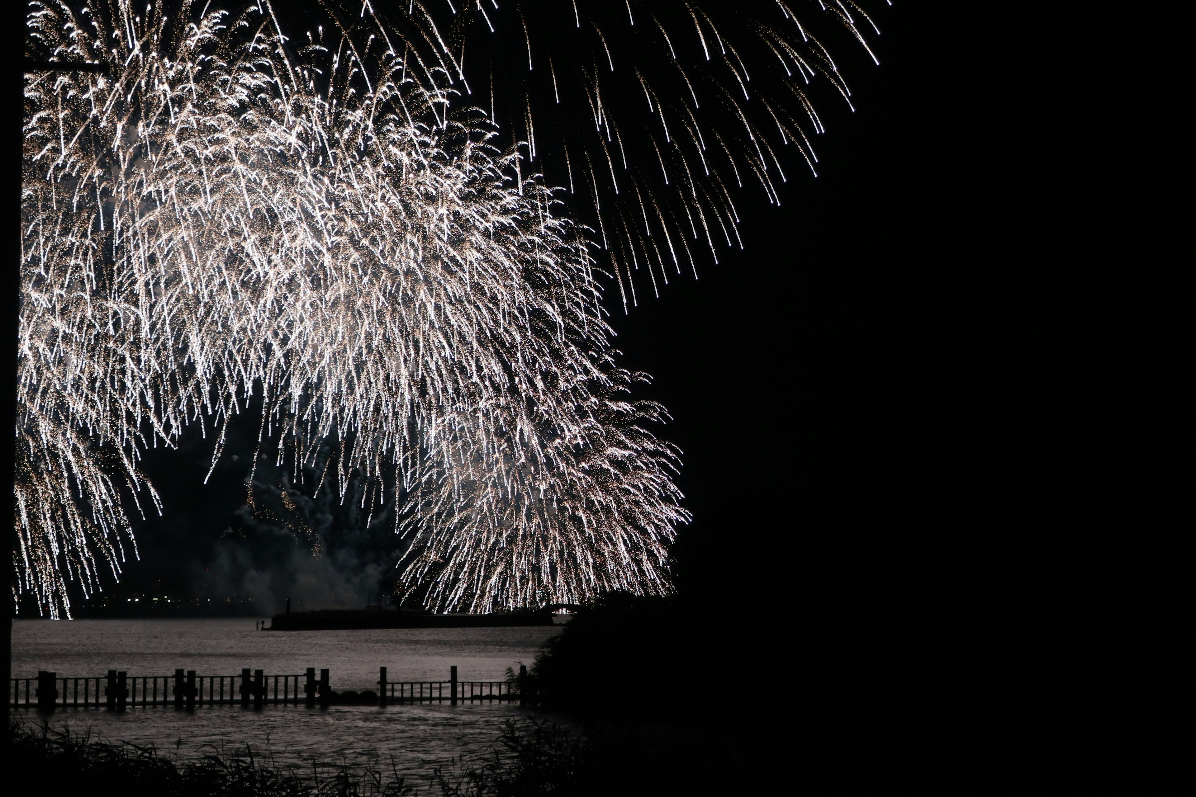 Arching white fireworks over a dark water surface at night