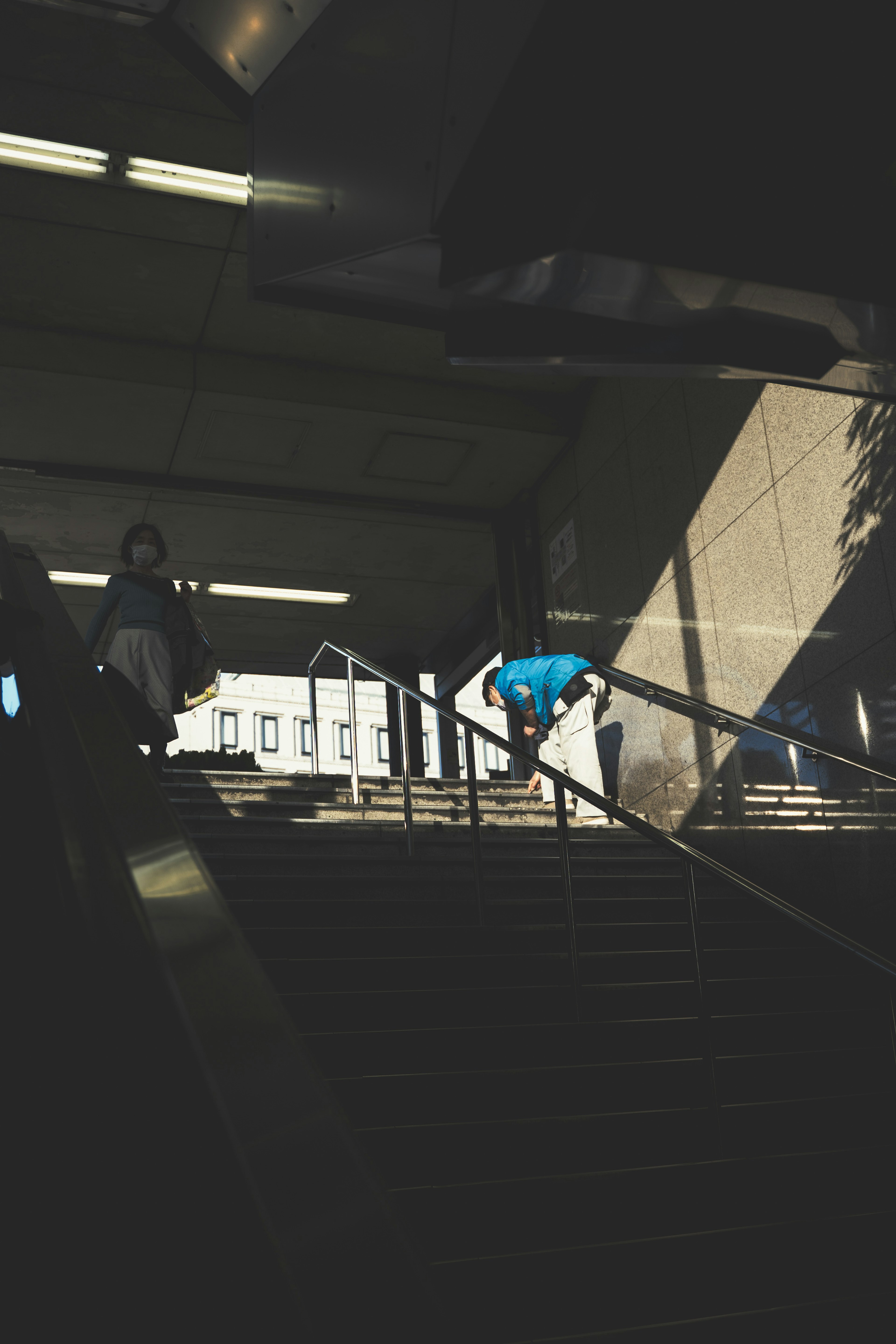 A person climbing stairs in a station with shadows and light