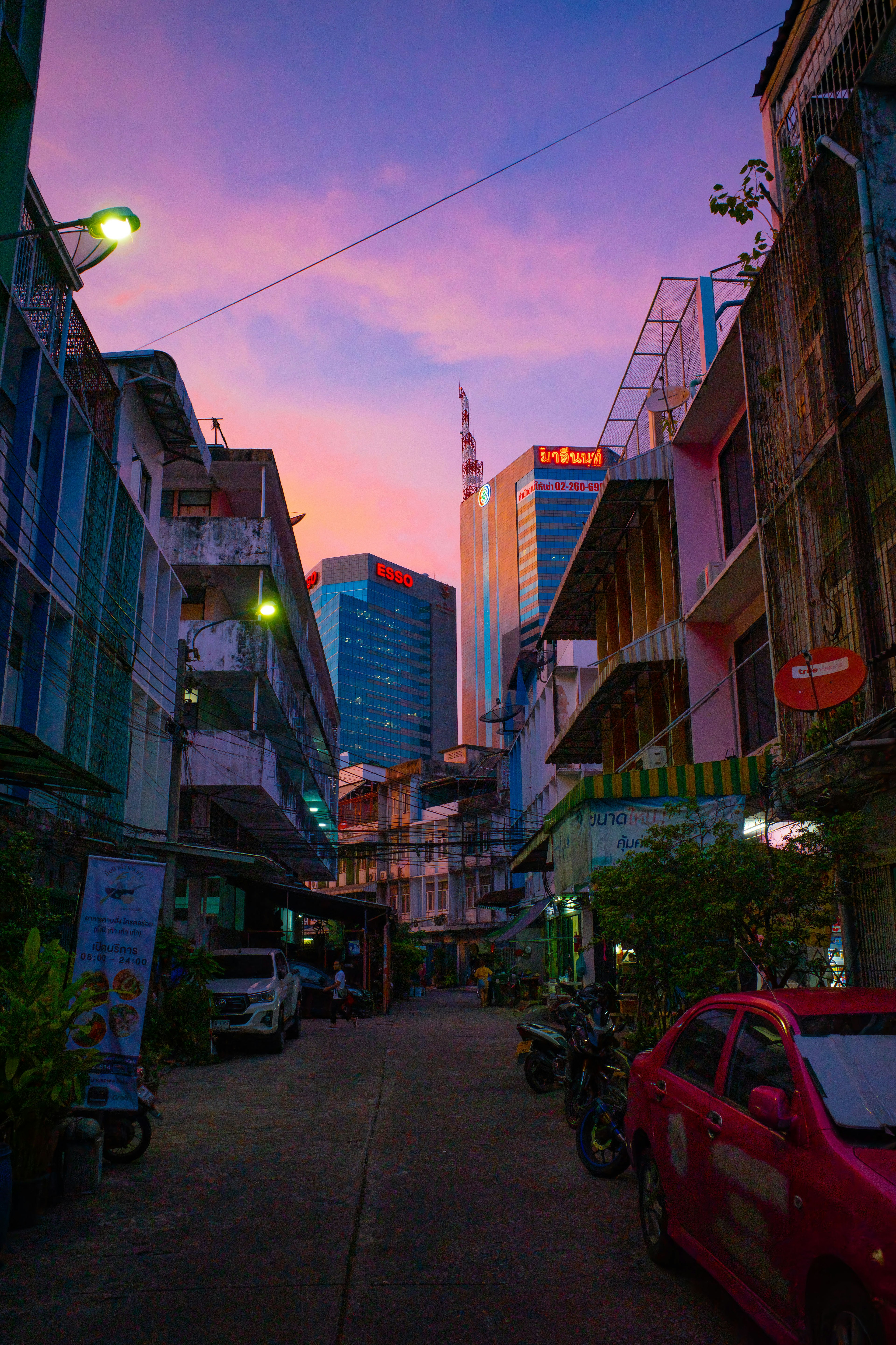 Jalan kota saat matahari terbenam dengan langit berwarna-warni bangunan dan mobil yang diparkir