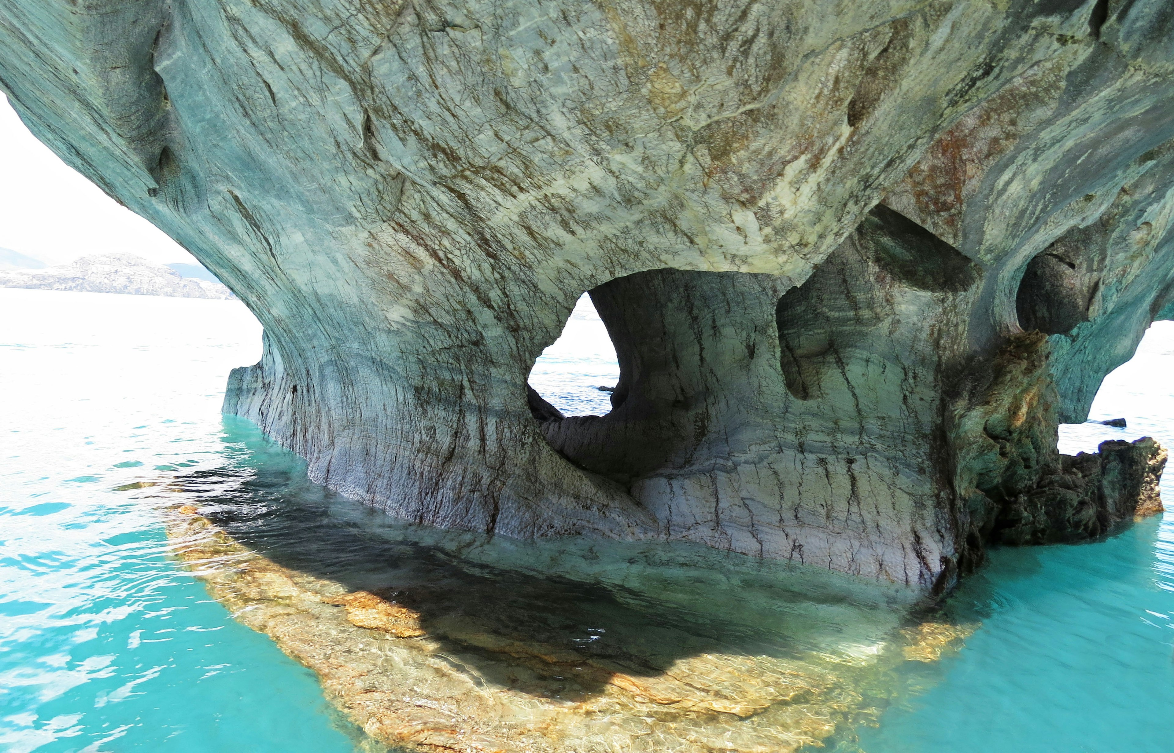 Photo of a large rock cave surrounded by clear blue water