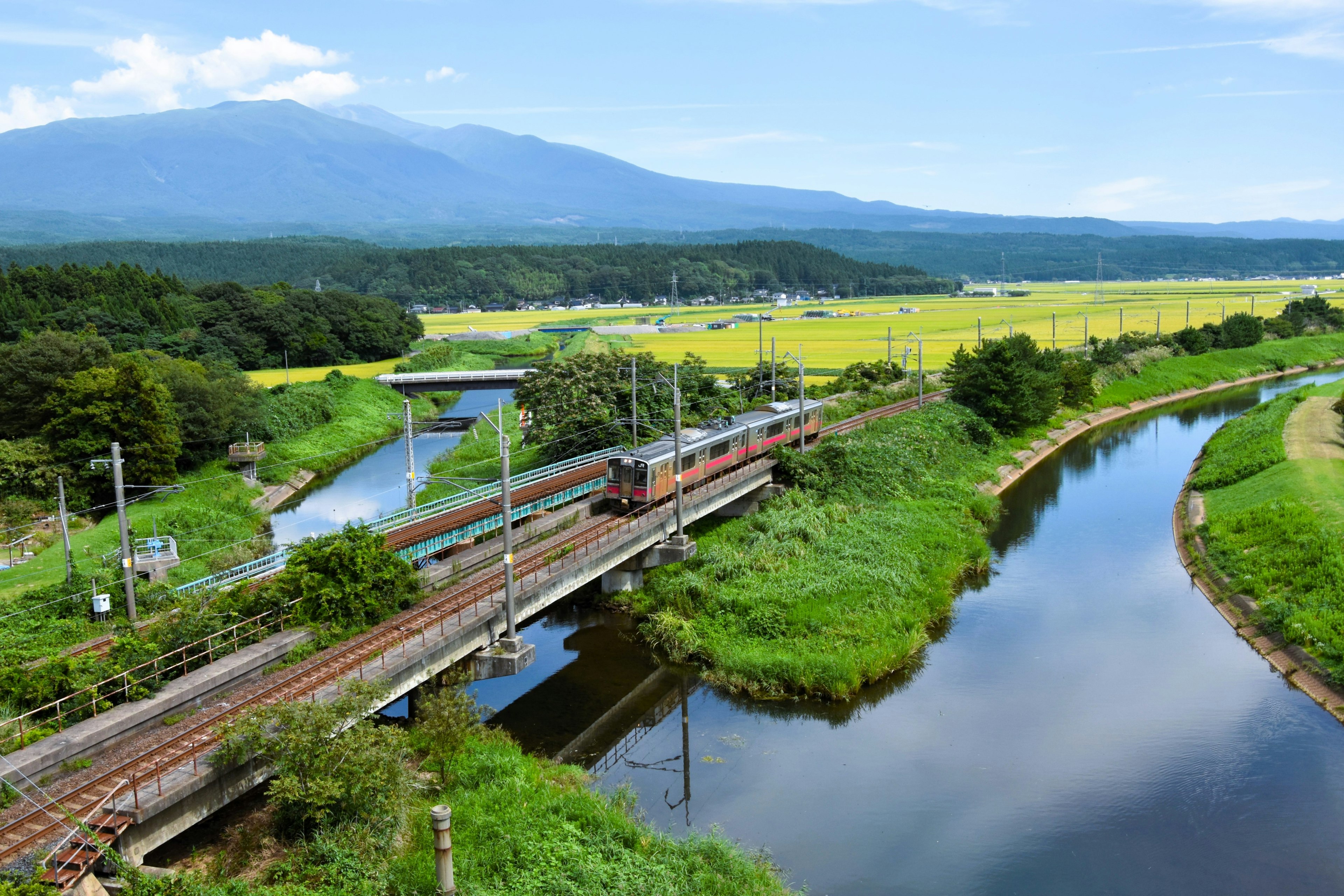 รถไฟวิ่งผ่านชนบทที่เขียวขจีโดยมีภูเขาเป็นฉากหลัง