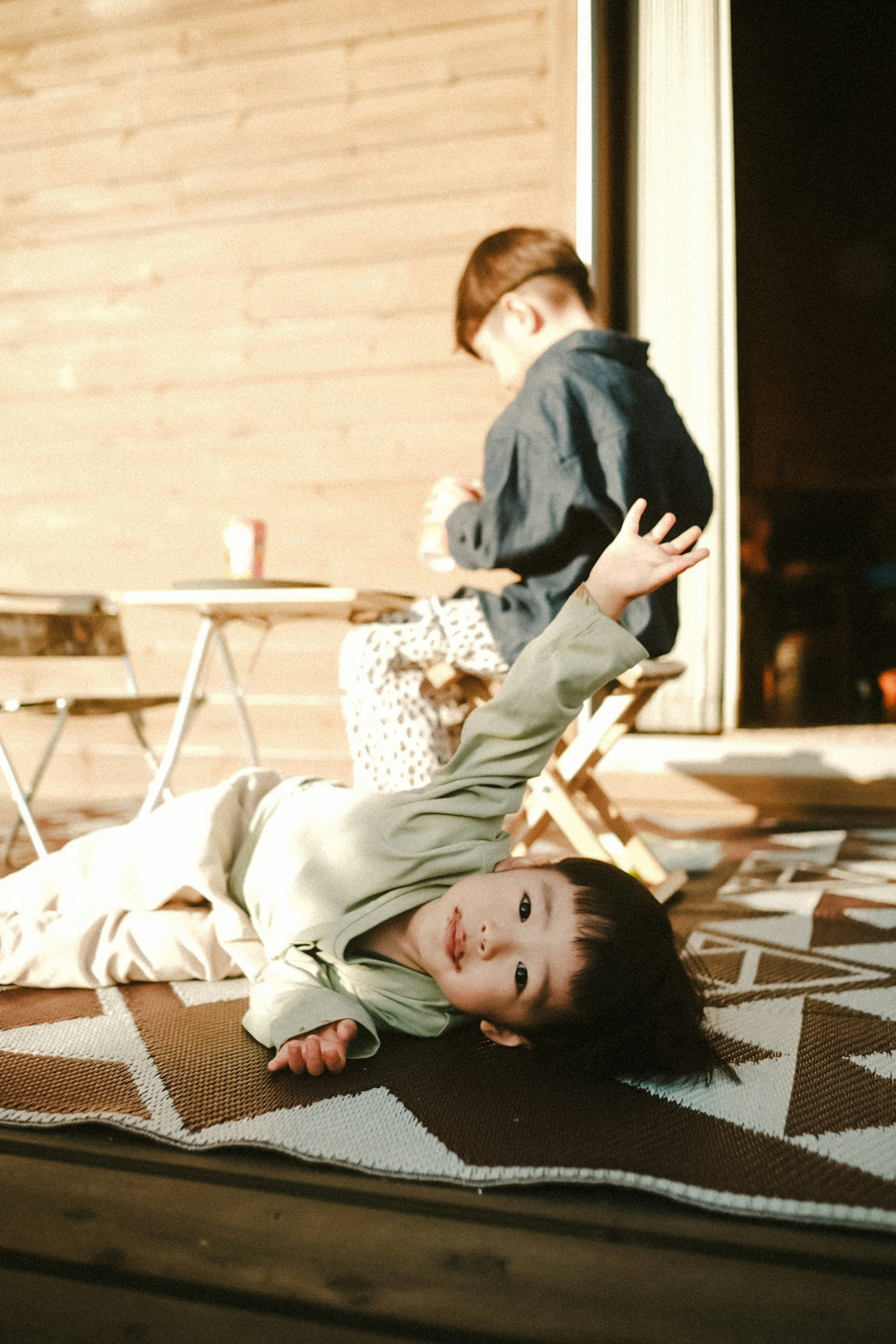 Zwei Kinder spielen im Freien Ein Kind liegt auf dem Boden mit einem Arm erhoben Ein anderes Kind steht und macht etwas