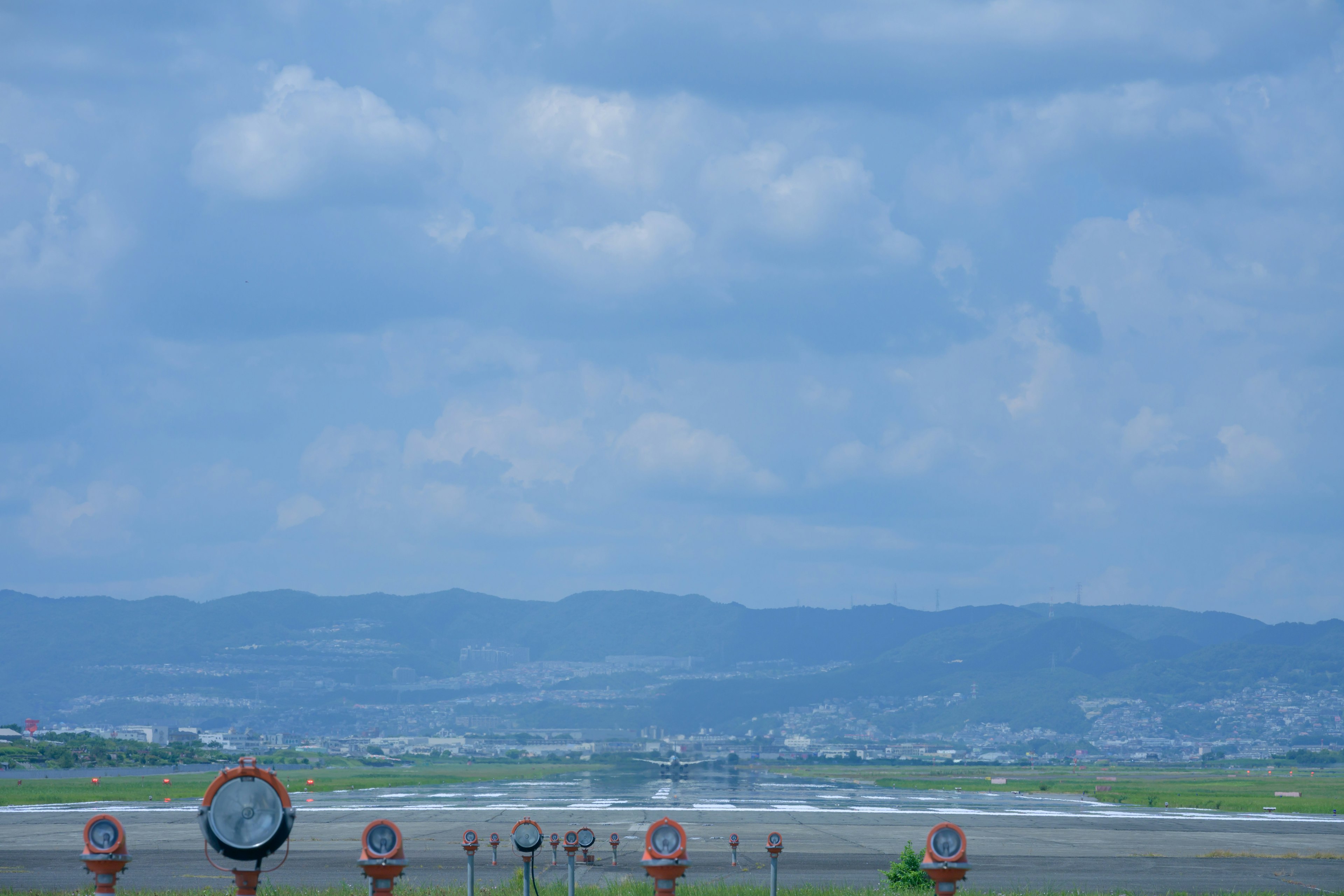 Airport runway under a blue sky with clouds and distant mountains visible