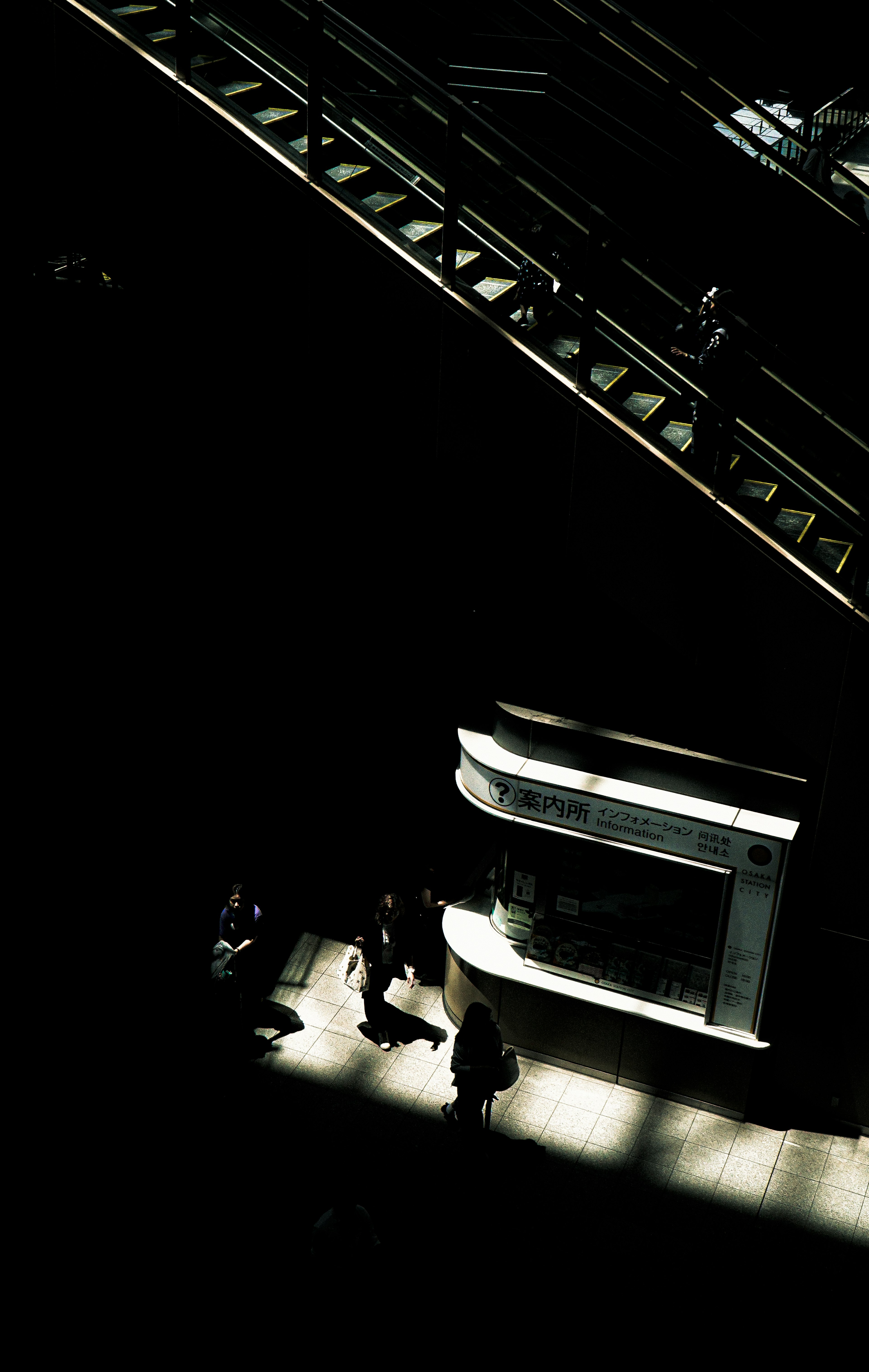 People walking in a dark setting with a bright escalator above