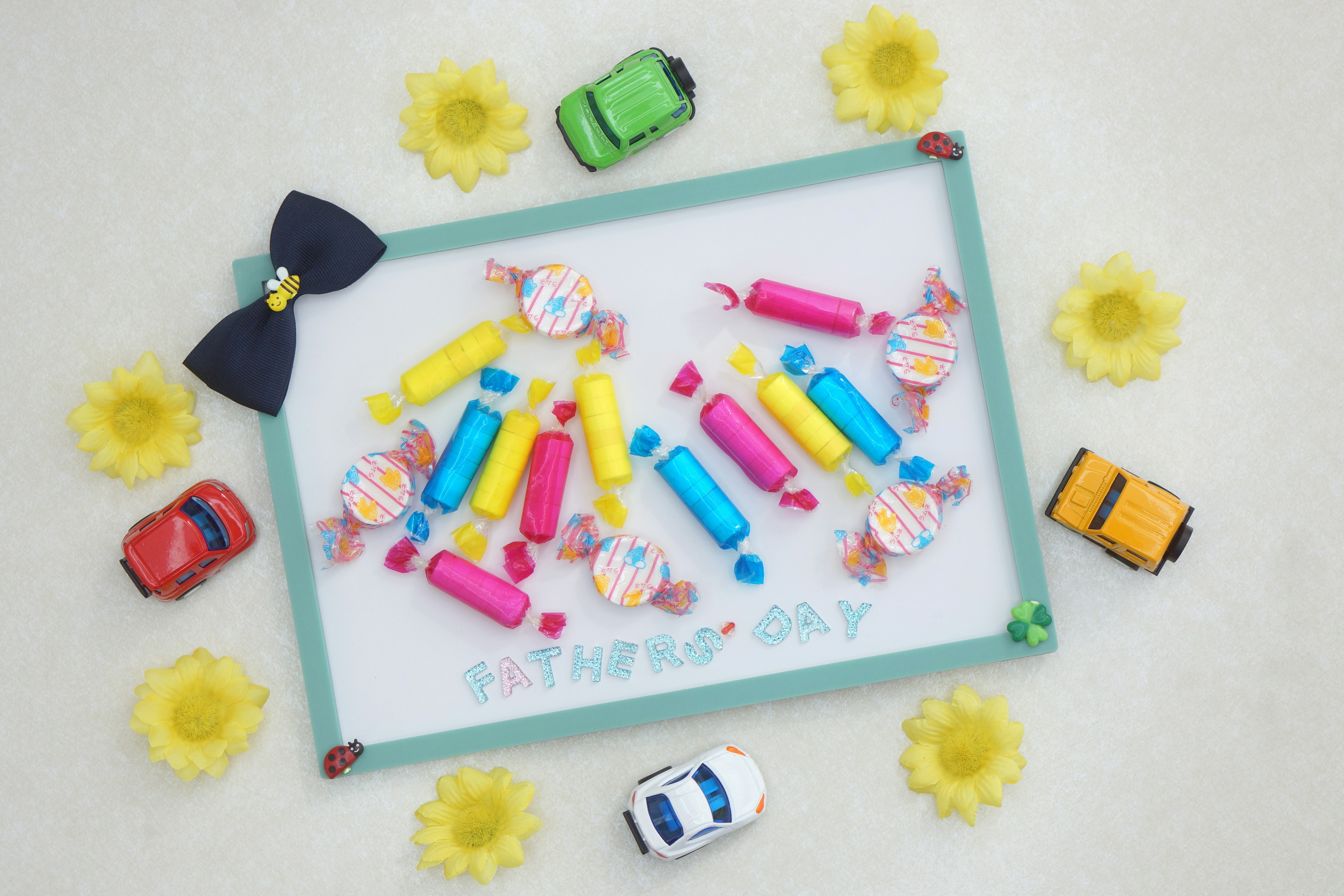 Bunte Bonbons und Spielzeugautos auf einer weißen Tafel umgeben von gelben Blumen angeordnet