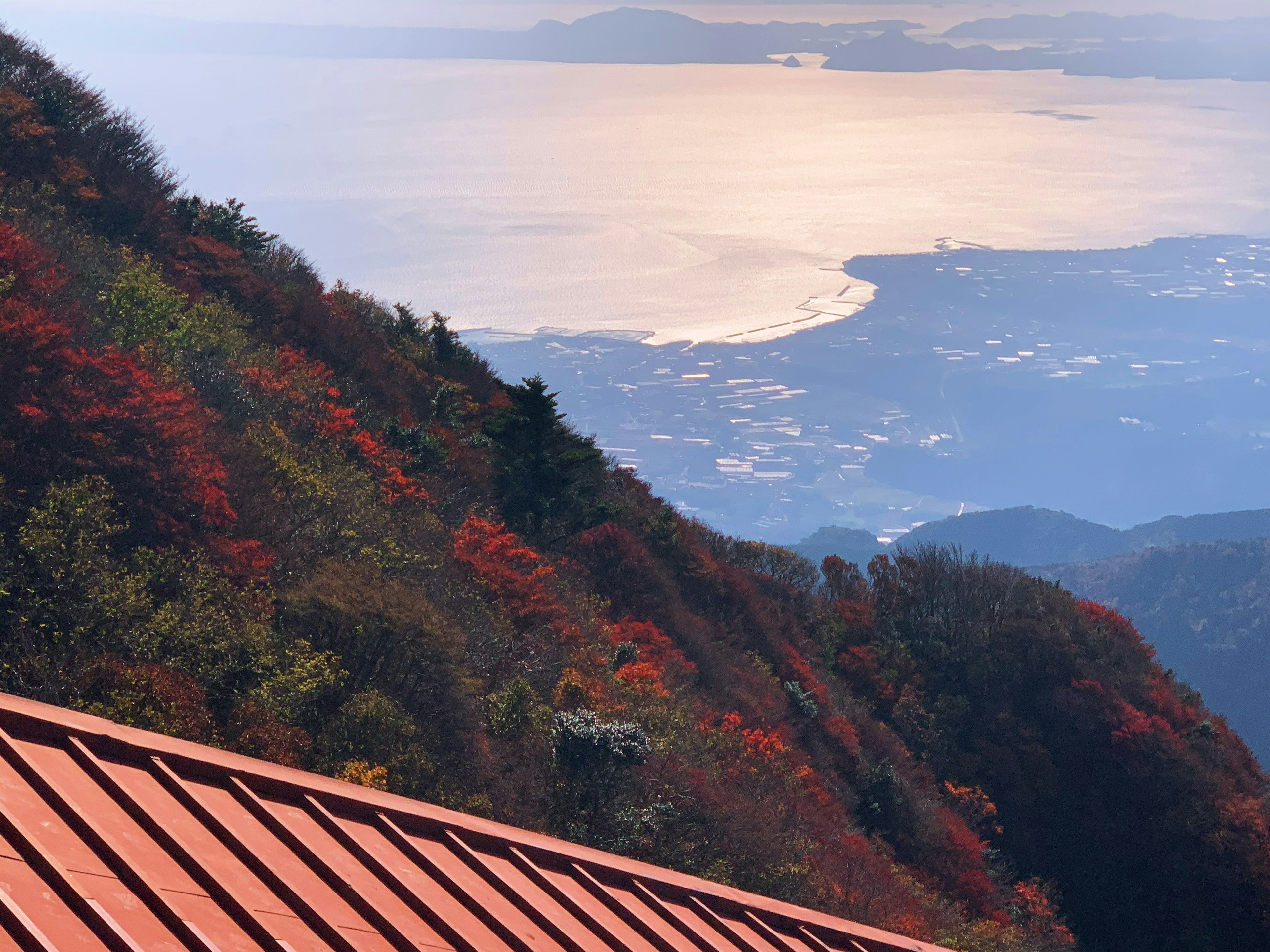 山の紅葉と海の景色を背景にした屋根