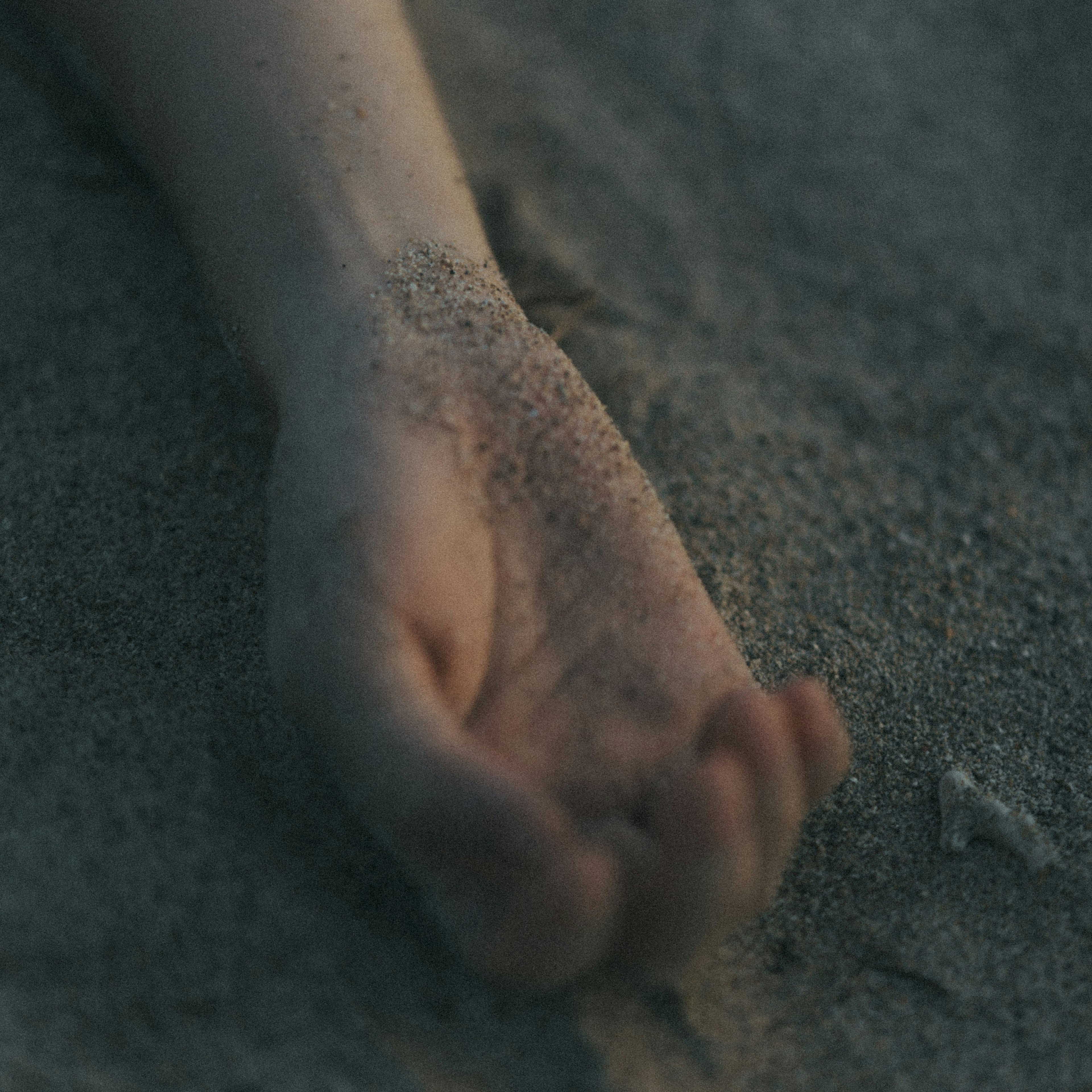 A hand partially buried in sand with a soft focus