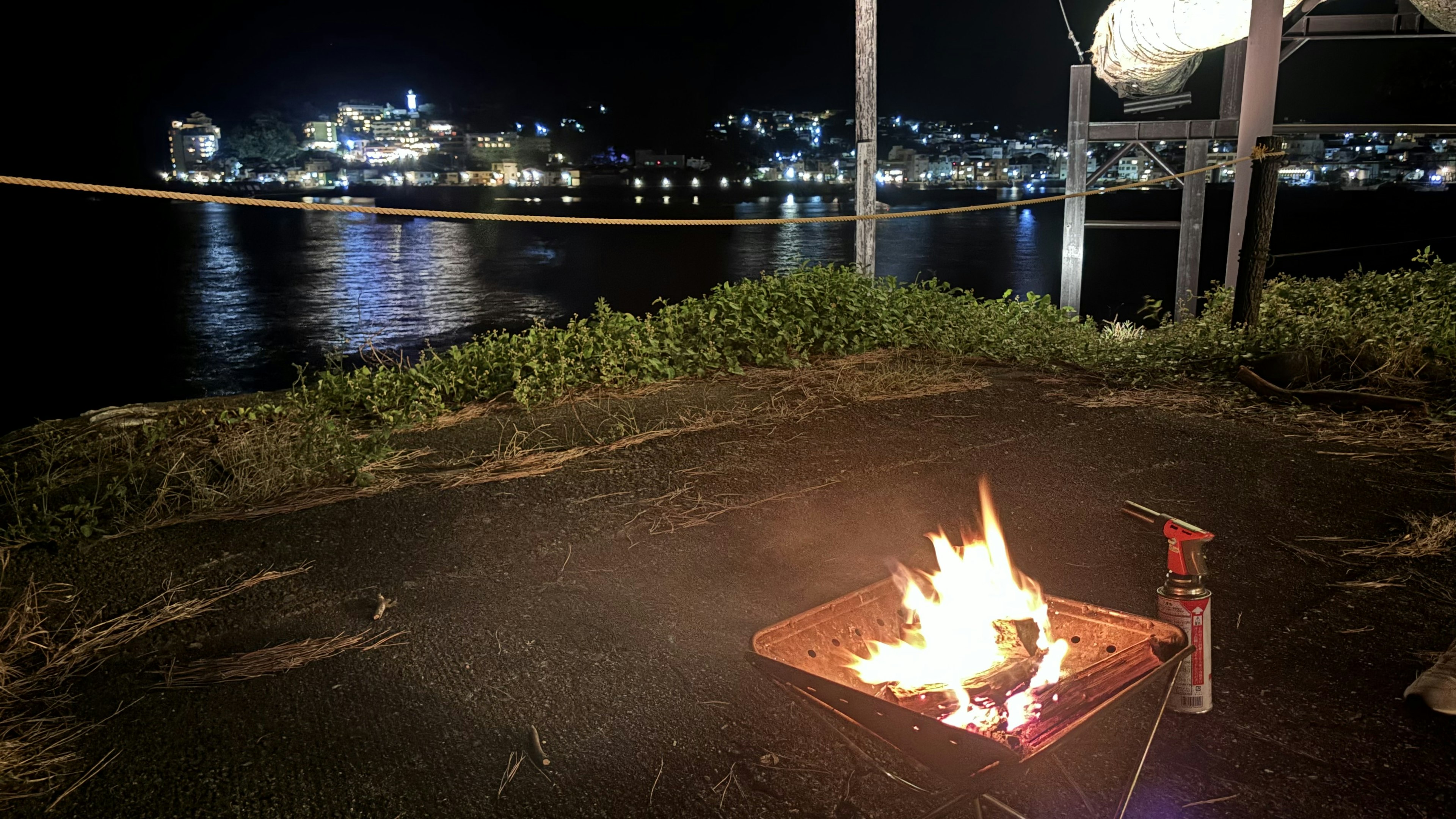 夜の海辺で燃える焚き火と遠くの街の明かり