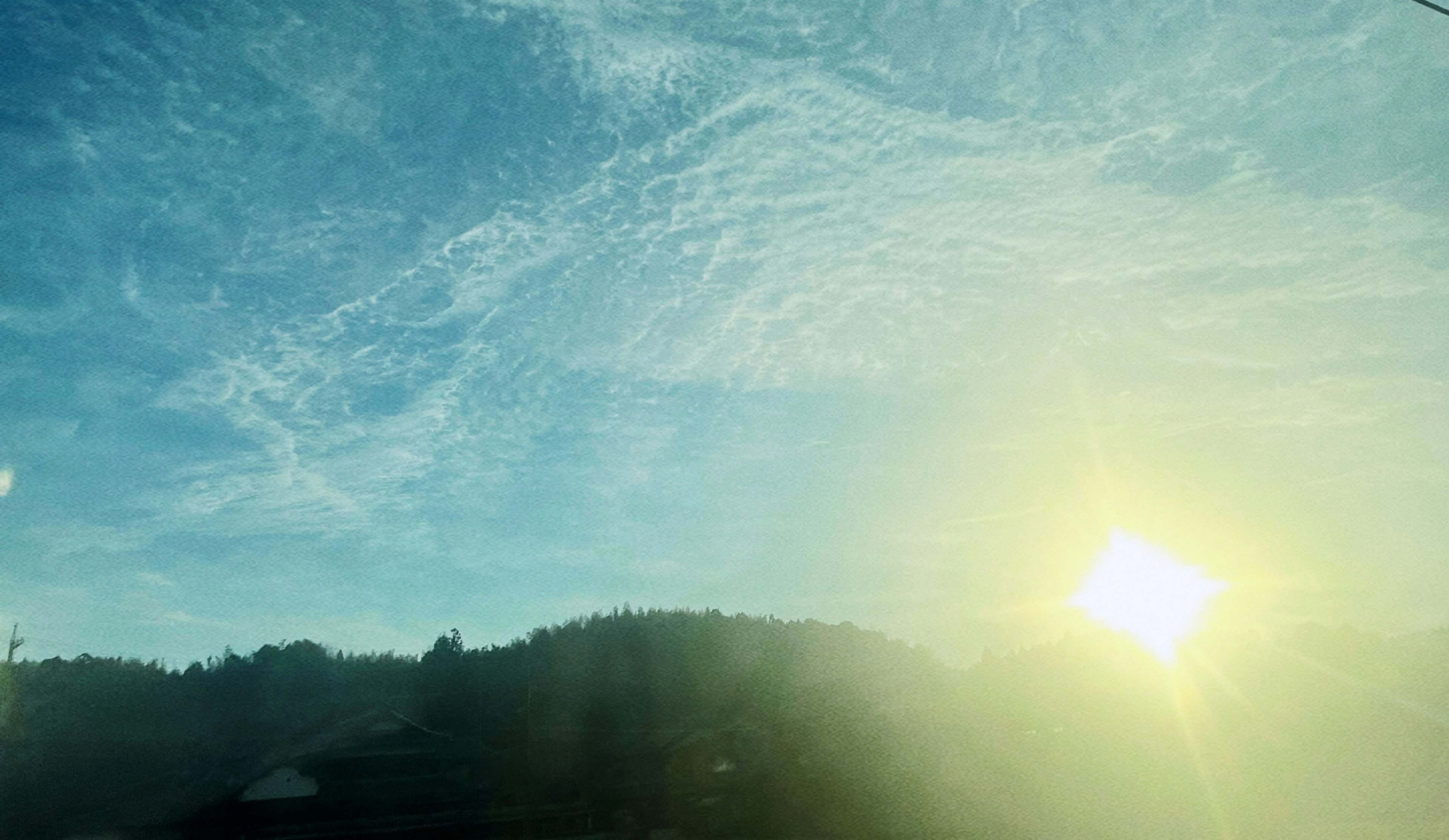 Brillante sol levantándose sobre montañas en silueta con cielo azul y nubes