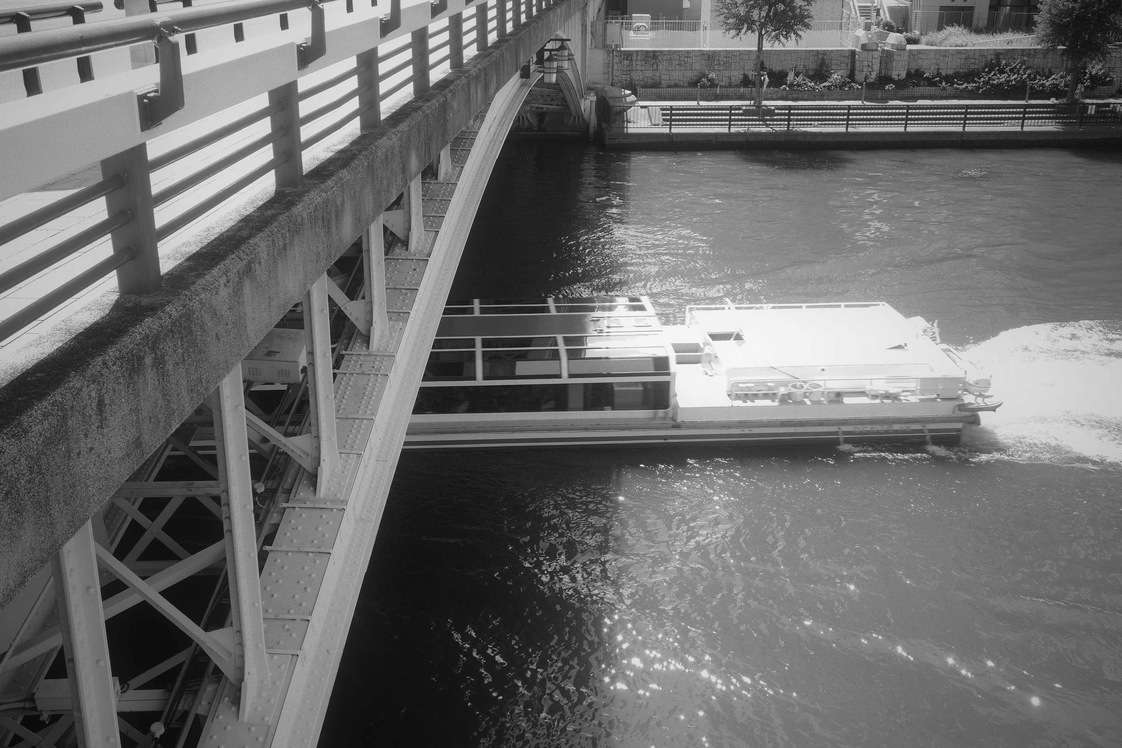 Vue en noir et blanc d'une rivière et d'un pont avec un bateau se déplaçant sur l'eau