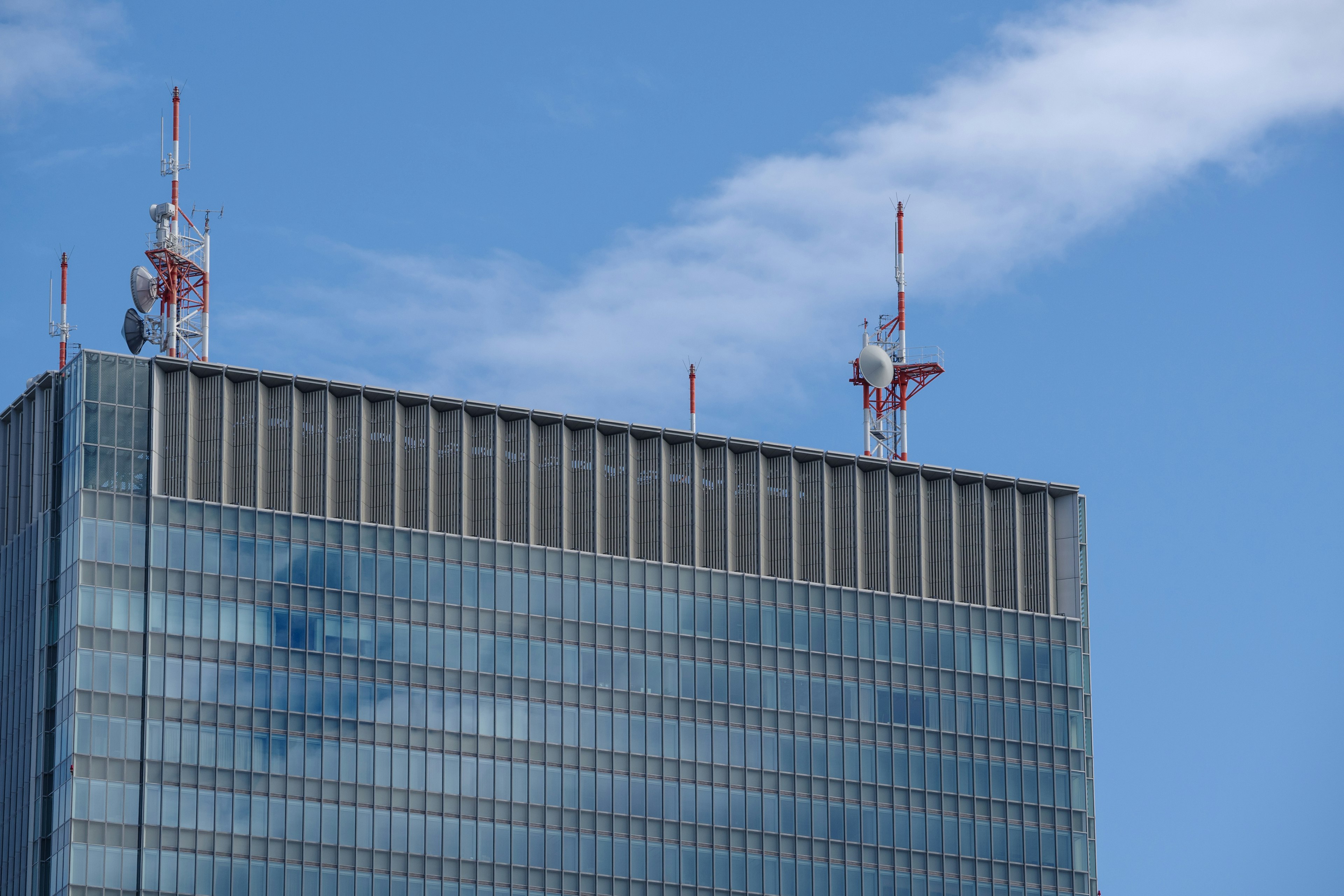 青空を背景にした高層ビルの上部にある通信アンテナ