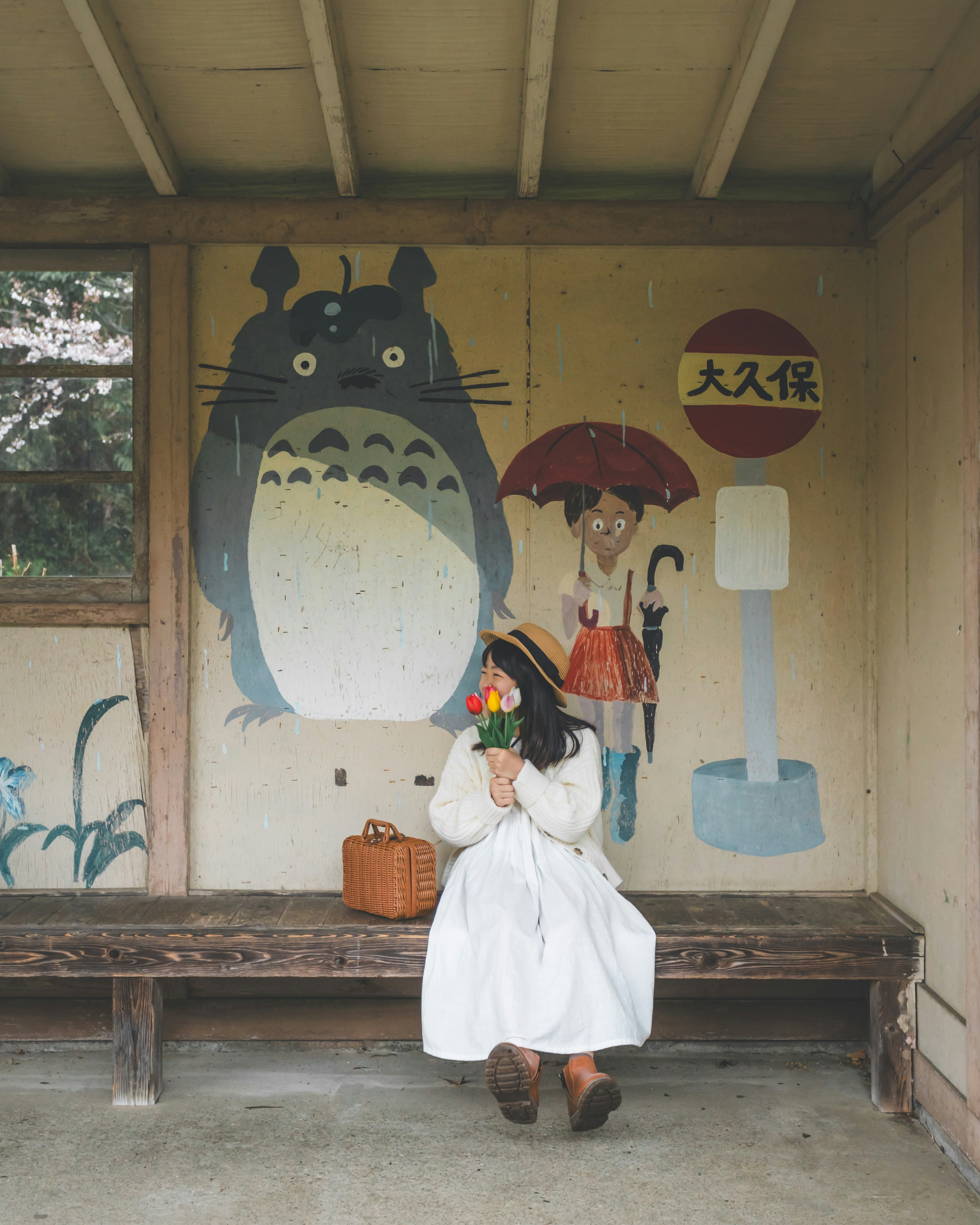 Une femme tenant des fleurs est assise devant une fresque de Totoro