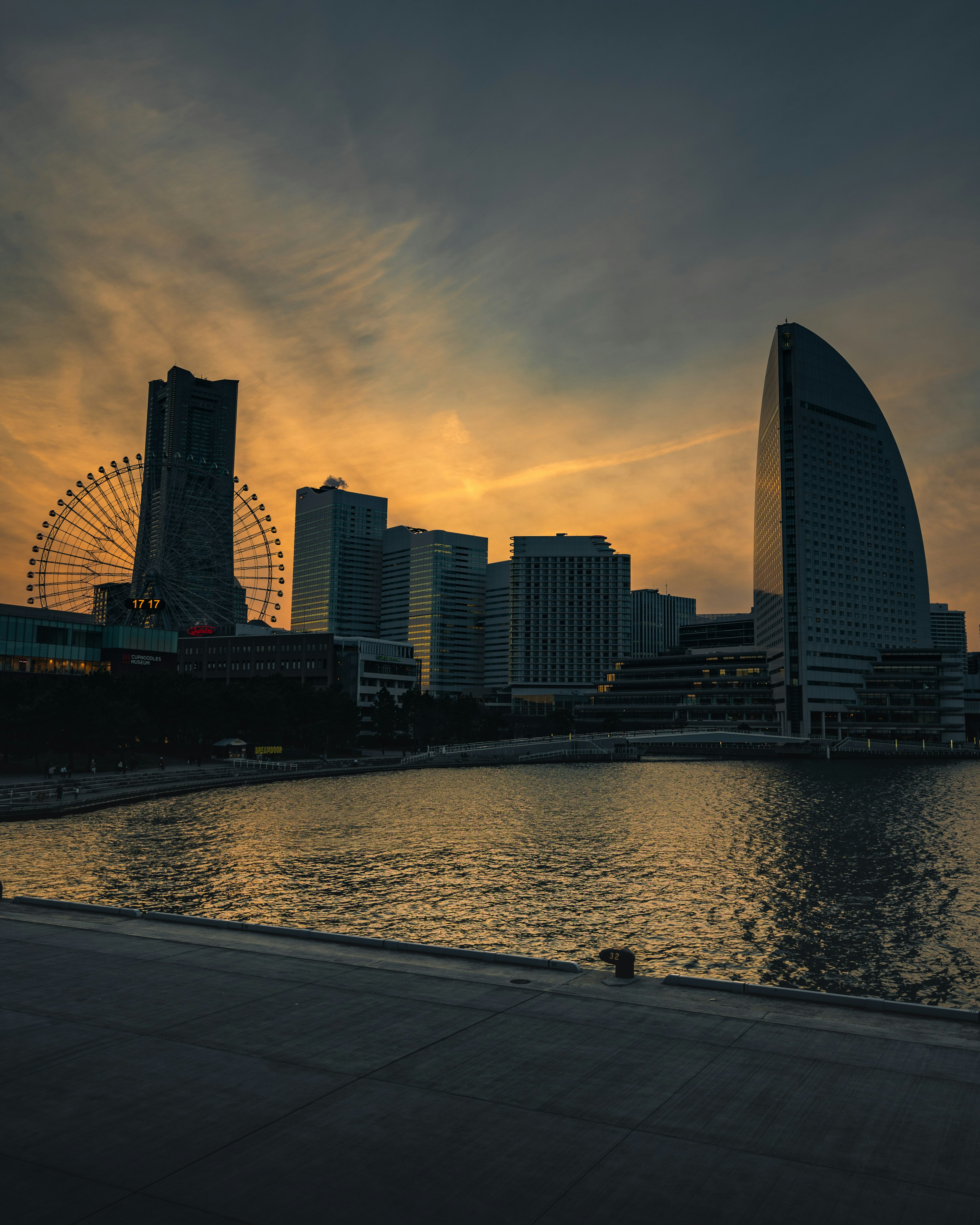 Siluet gedung pencakar langit dan roda ferris saat senja di tepi laut Yokohama