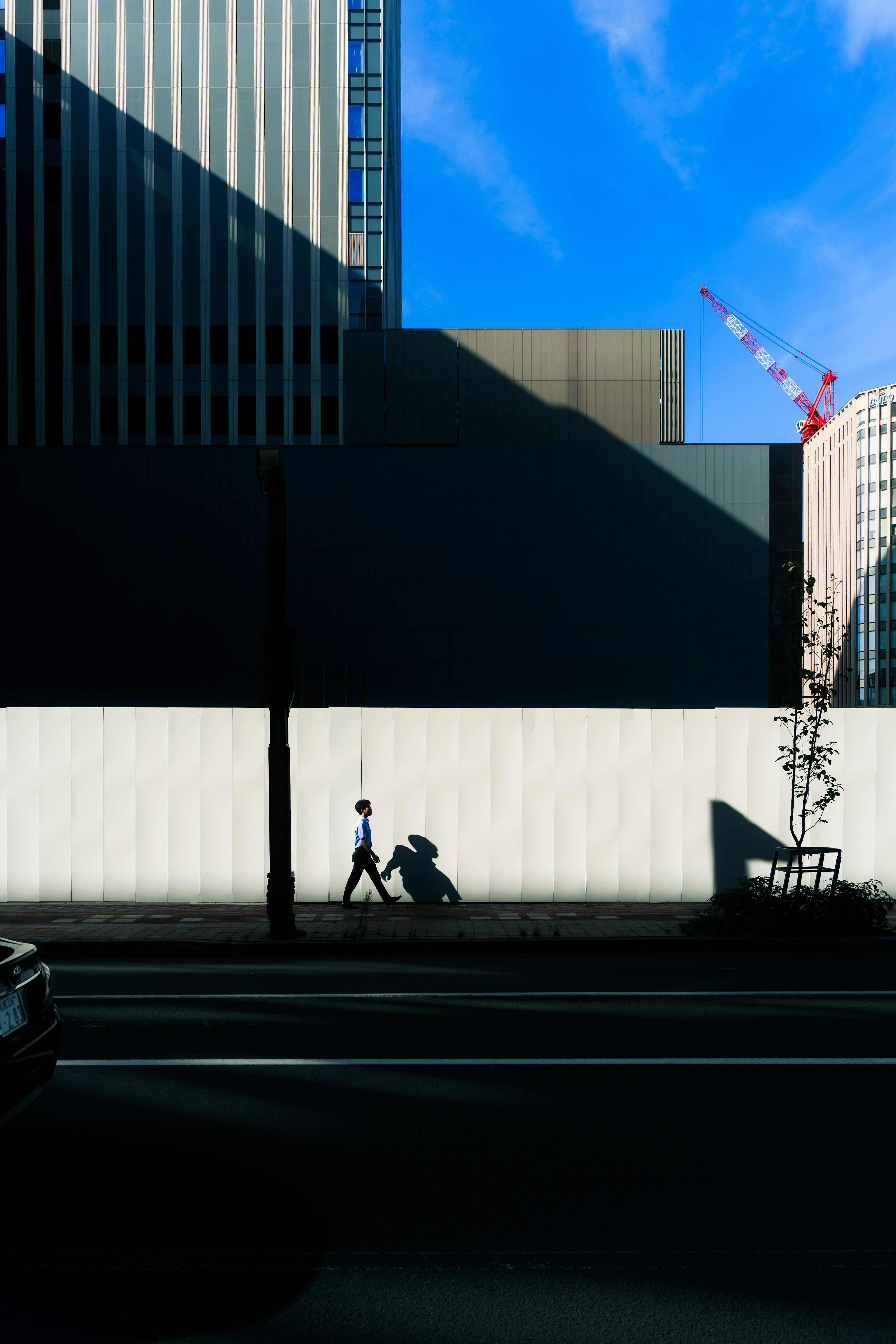 Silhouette of a person walking with a bicycle against a backdrop of buildings and blue sky