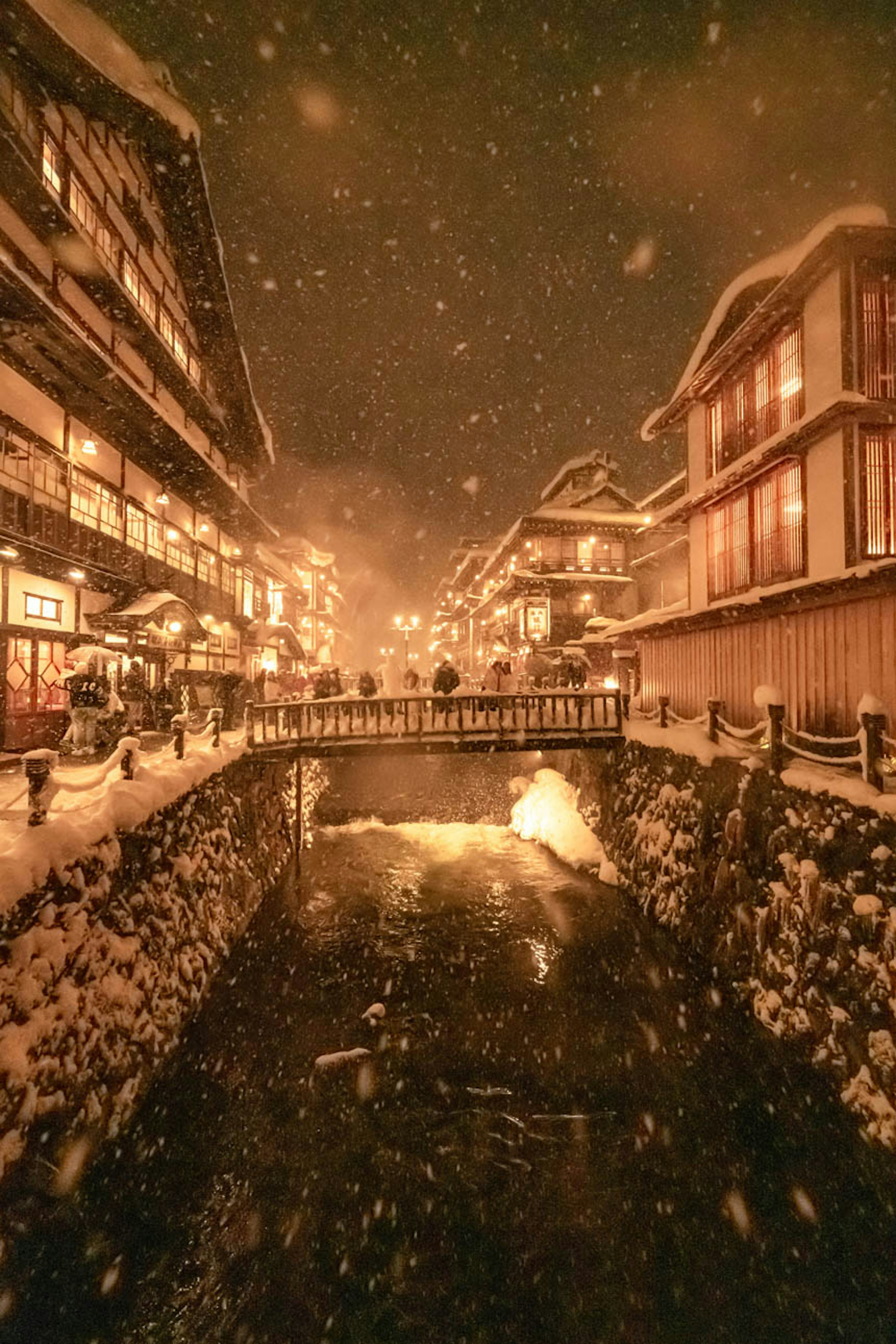 Snow-covered landscape with warmly lit buildings along a canal