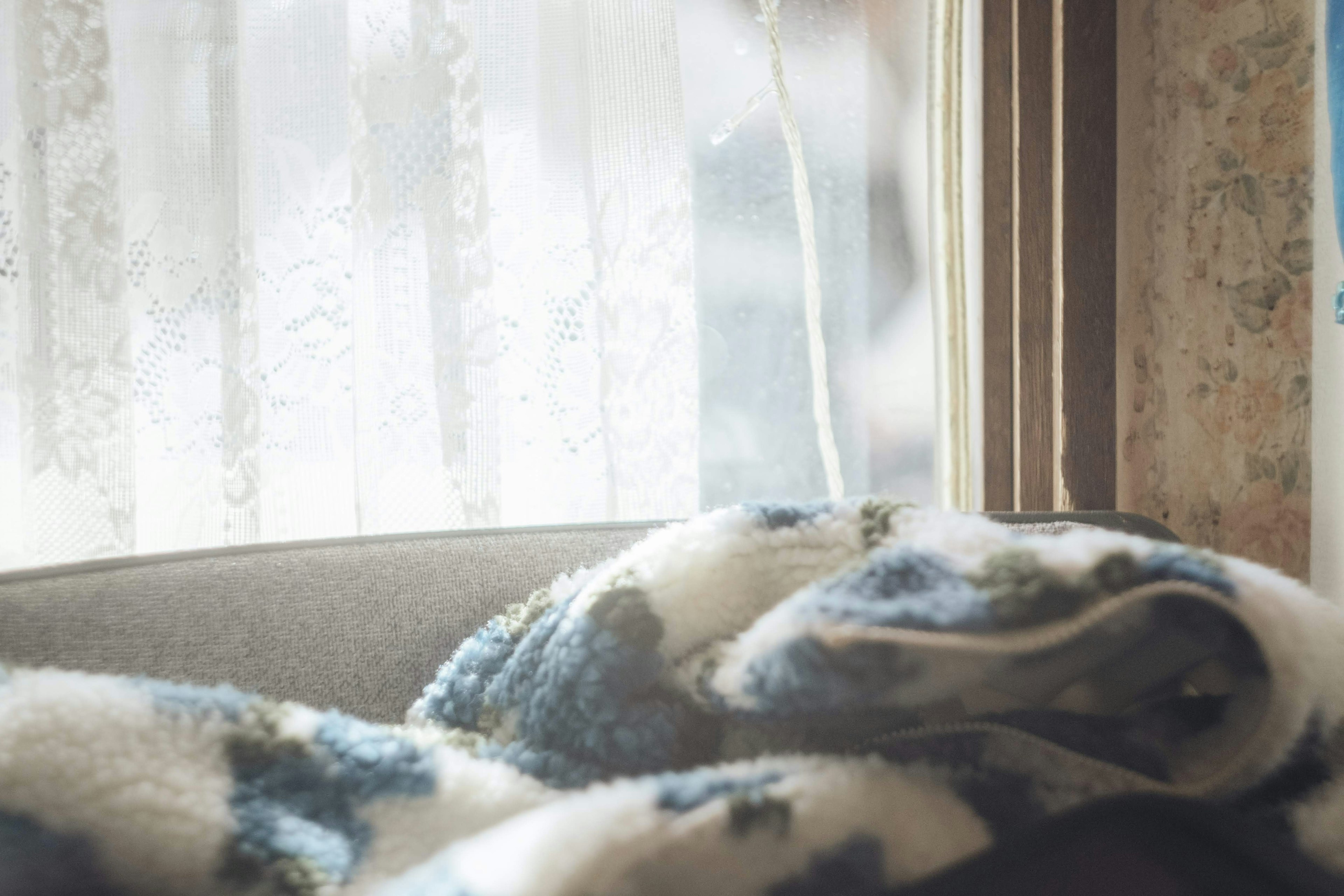 A blue and white patterned blanket draped near a window with sheer curtains