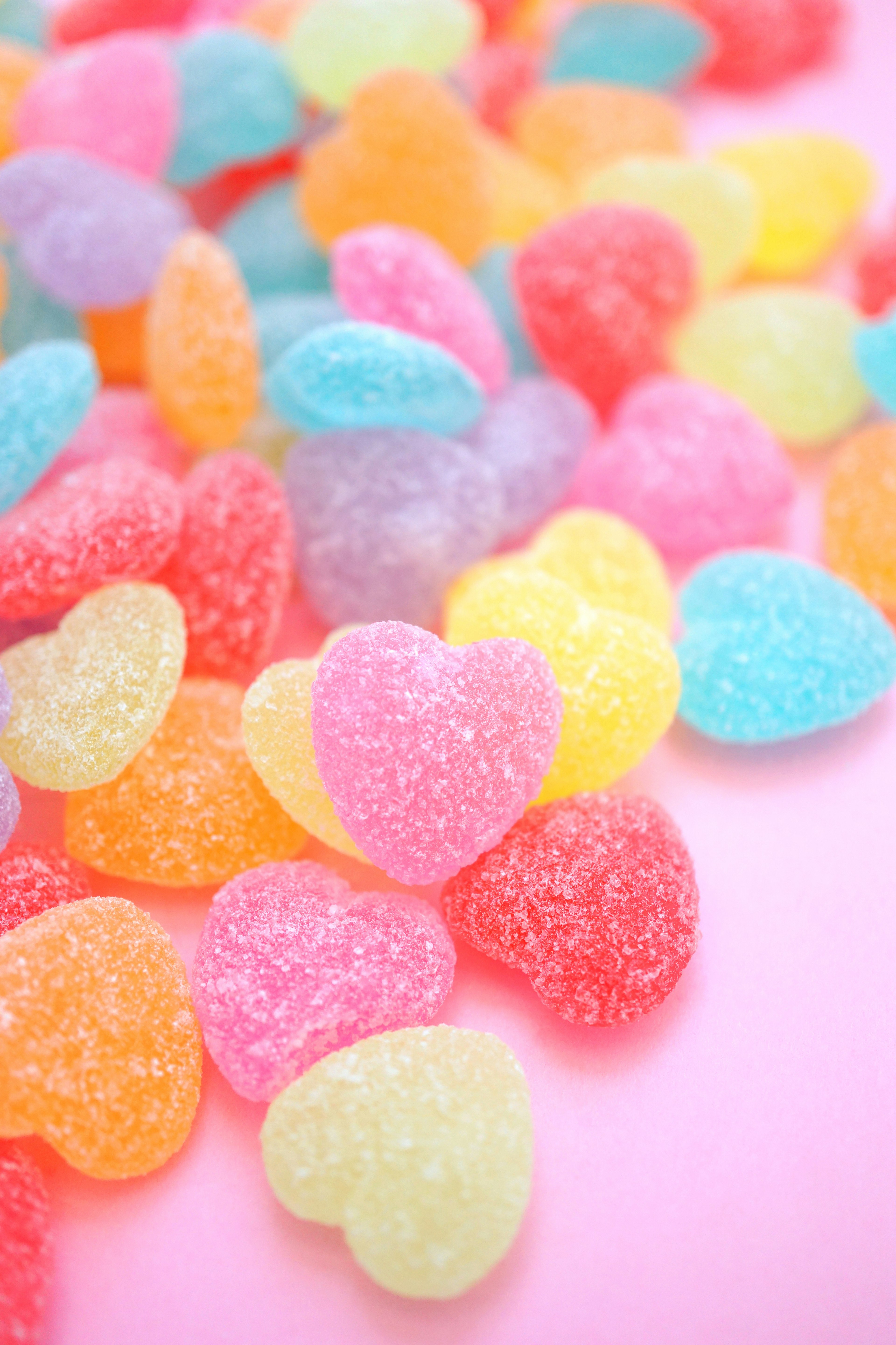 Caramelos de goma en forma de corazón de colores esparcidos sobre un fondo rosa