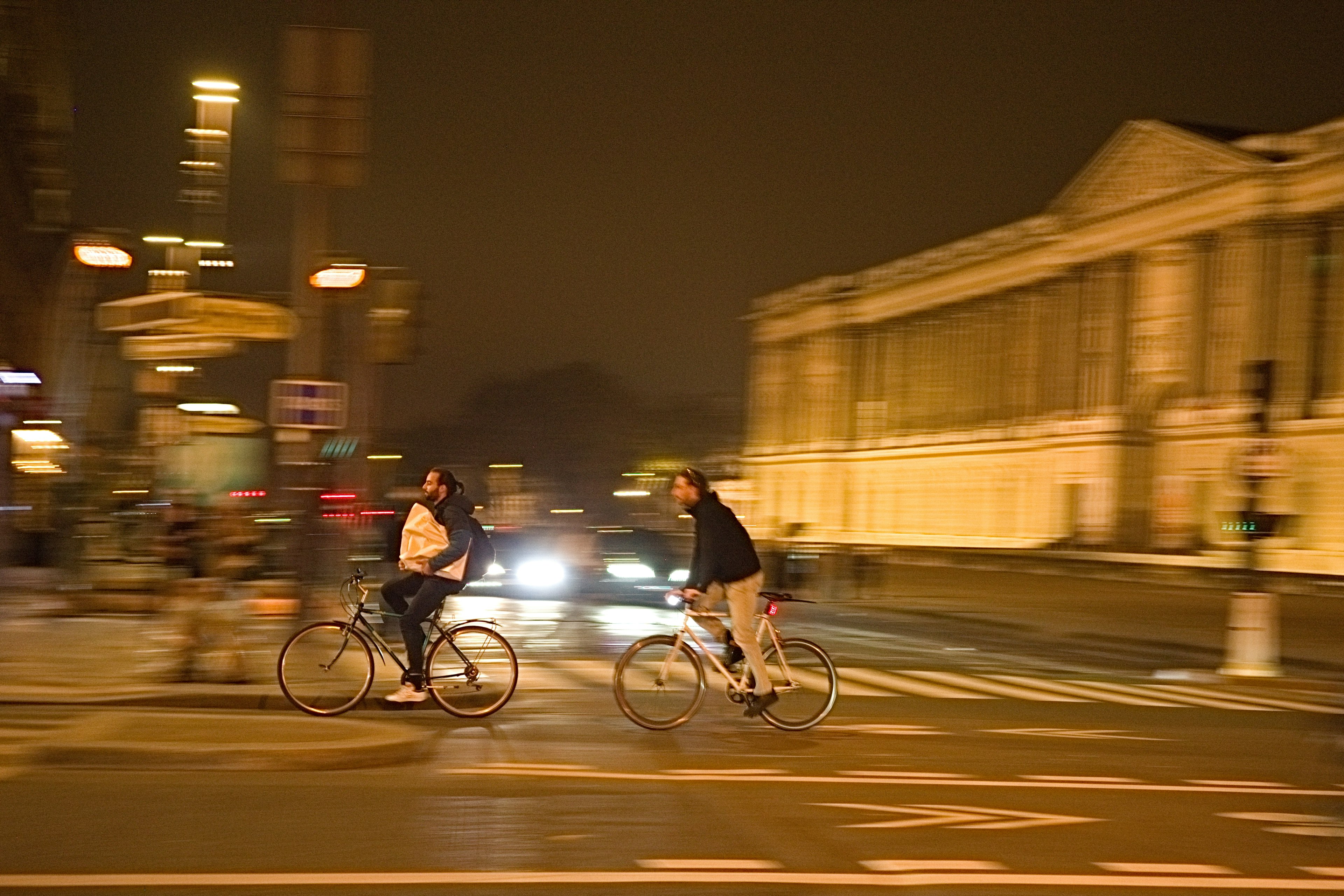 Deux hommes à vélo dans la ville la nuit avec des bâtiments illuminés