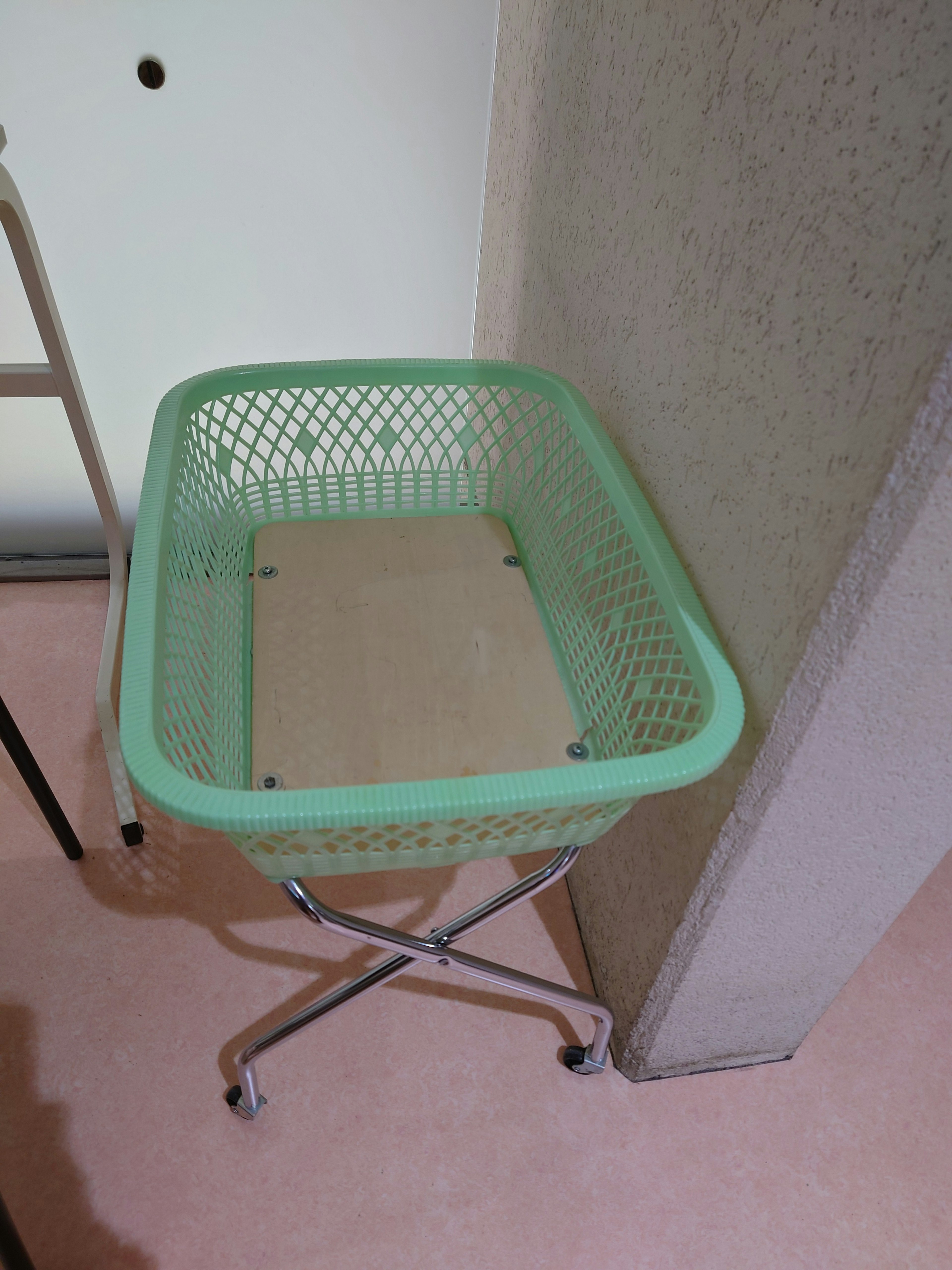 Una cesta de plástico verde sobre un soporte de metal con un suelo rosa claro