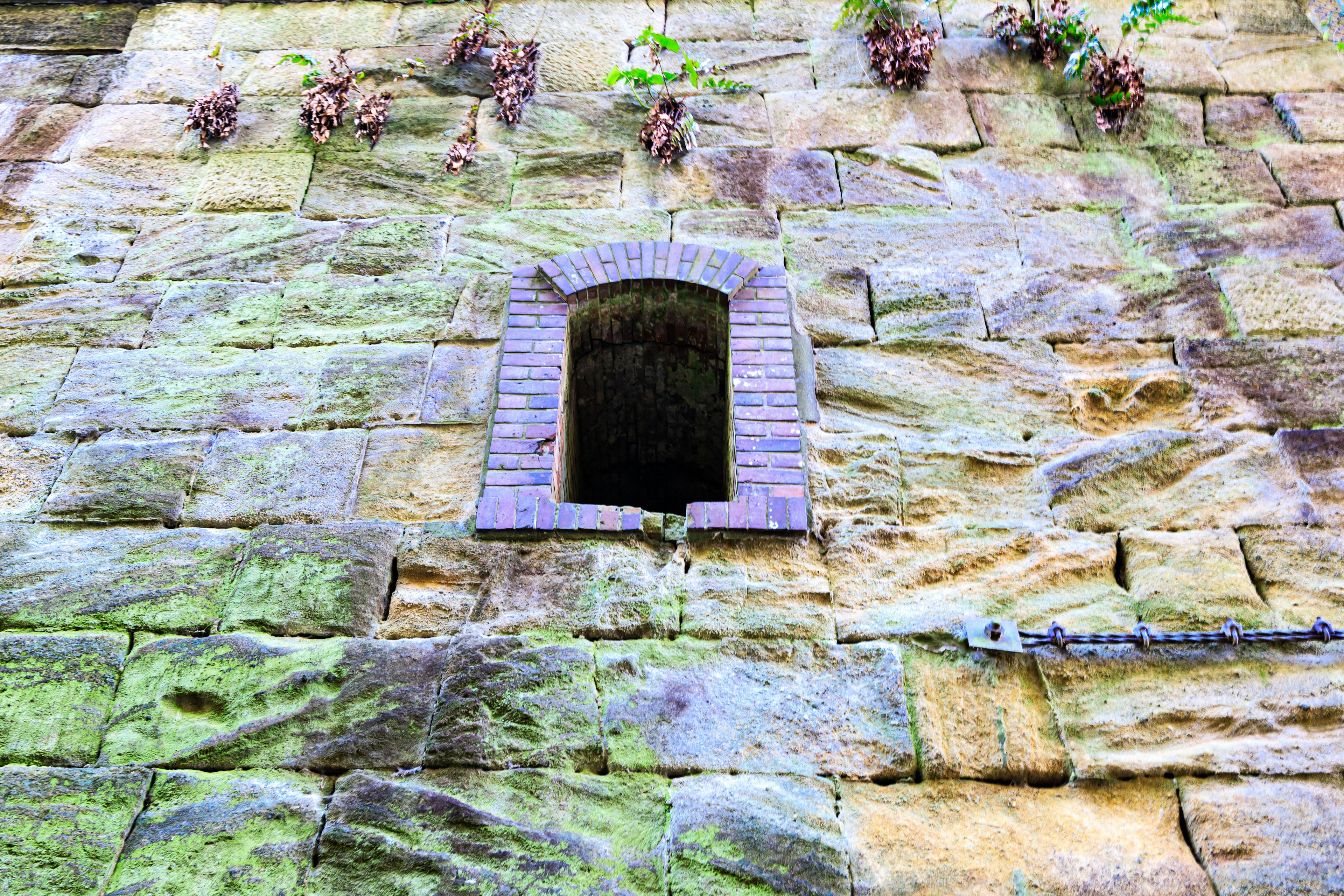 Kleines Fenster in einer alten Steinfassade mit Moos bedeckt