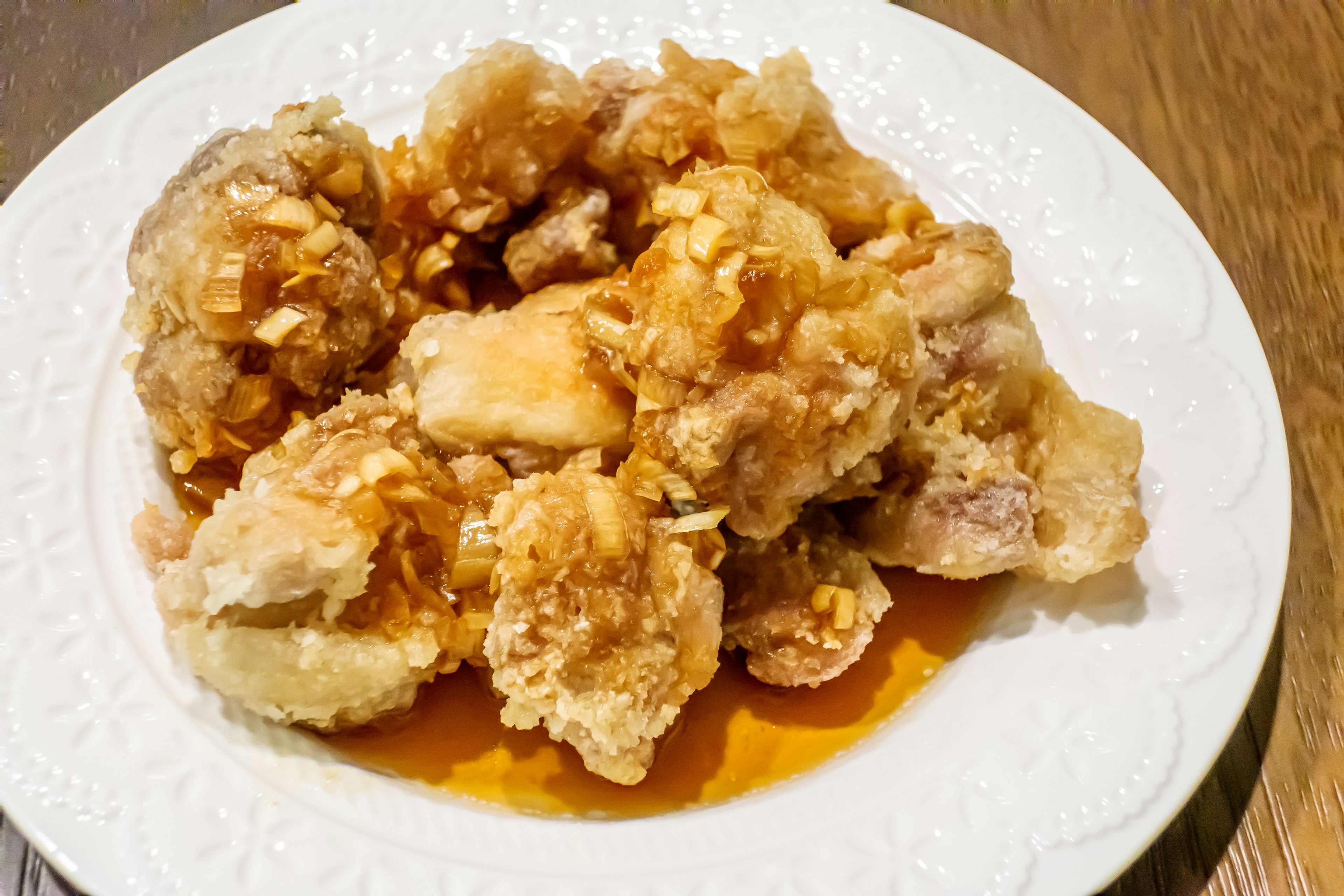 Trozos de pollo frito cubiertos con salsa dulce servidos en un plato blanco