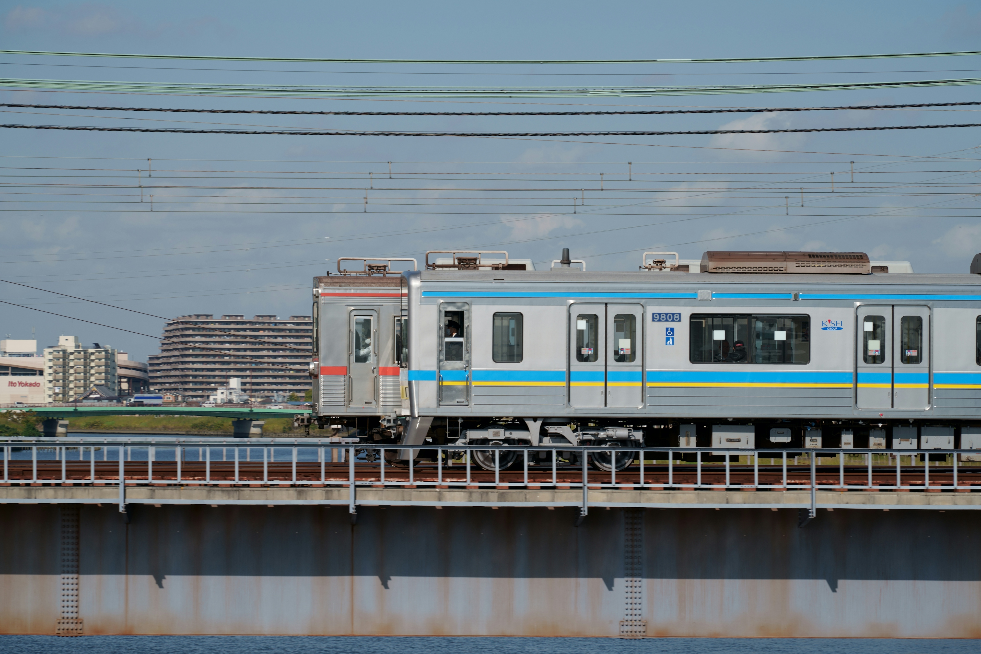 A blue train crossing a bridge against a clear sky