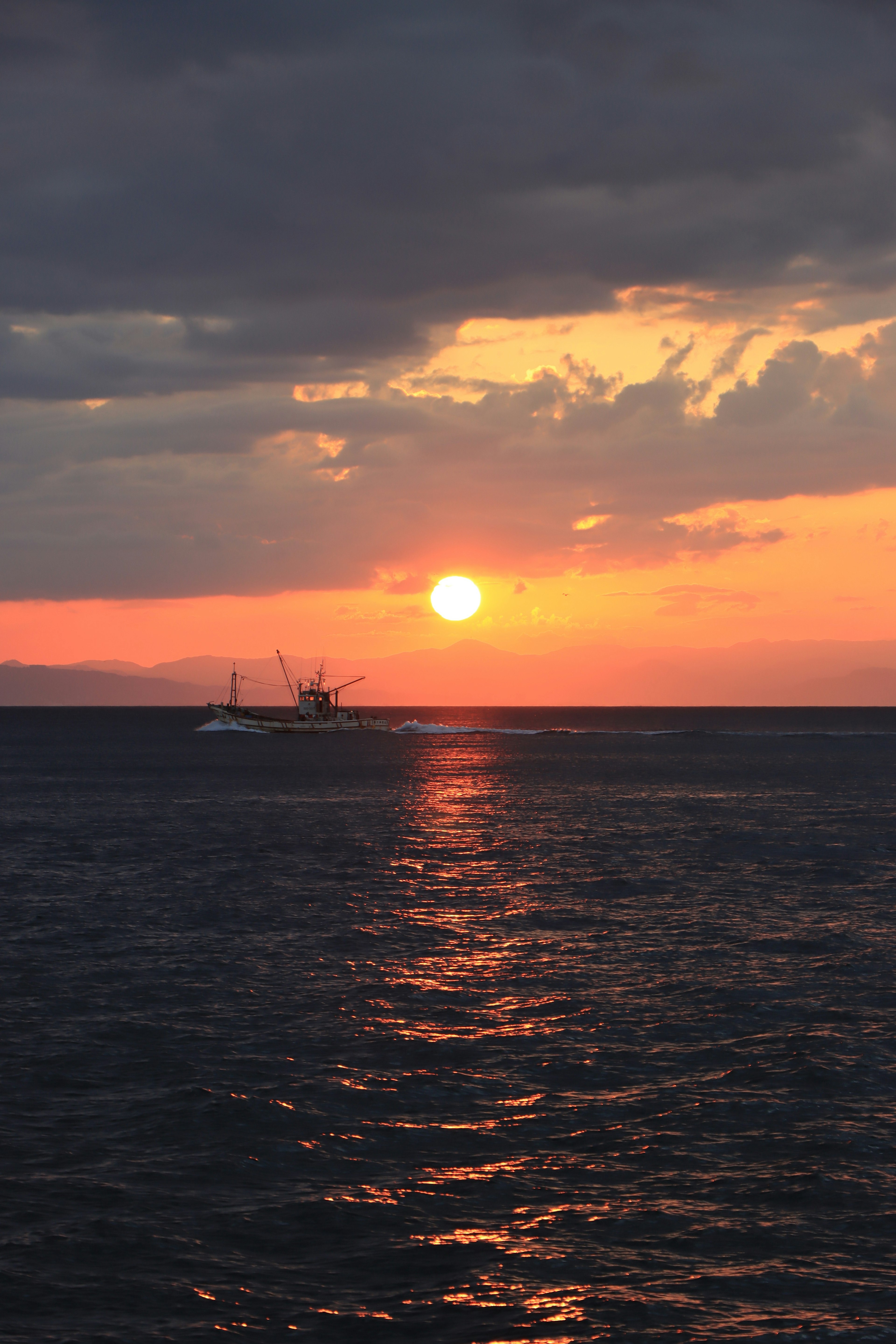 Schöner Sonnenuntergang, der sich im Ozean spiegelt, mit einem Boot in der Ferne