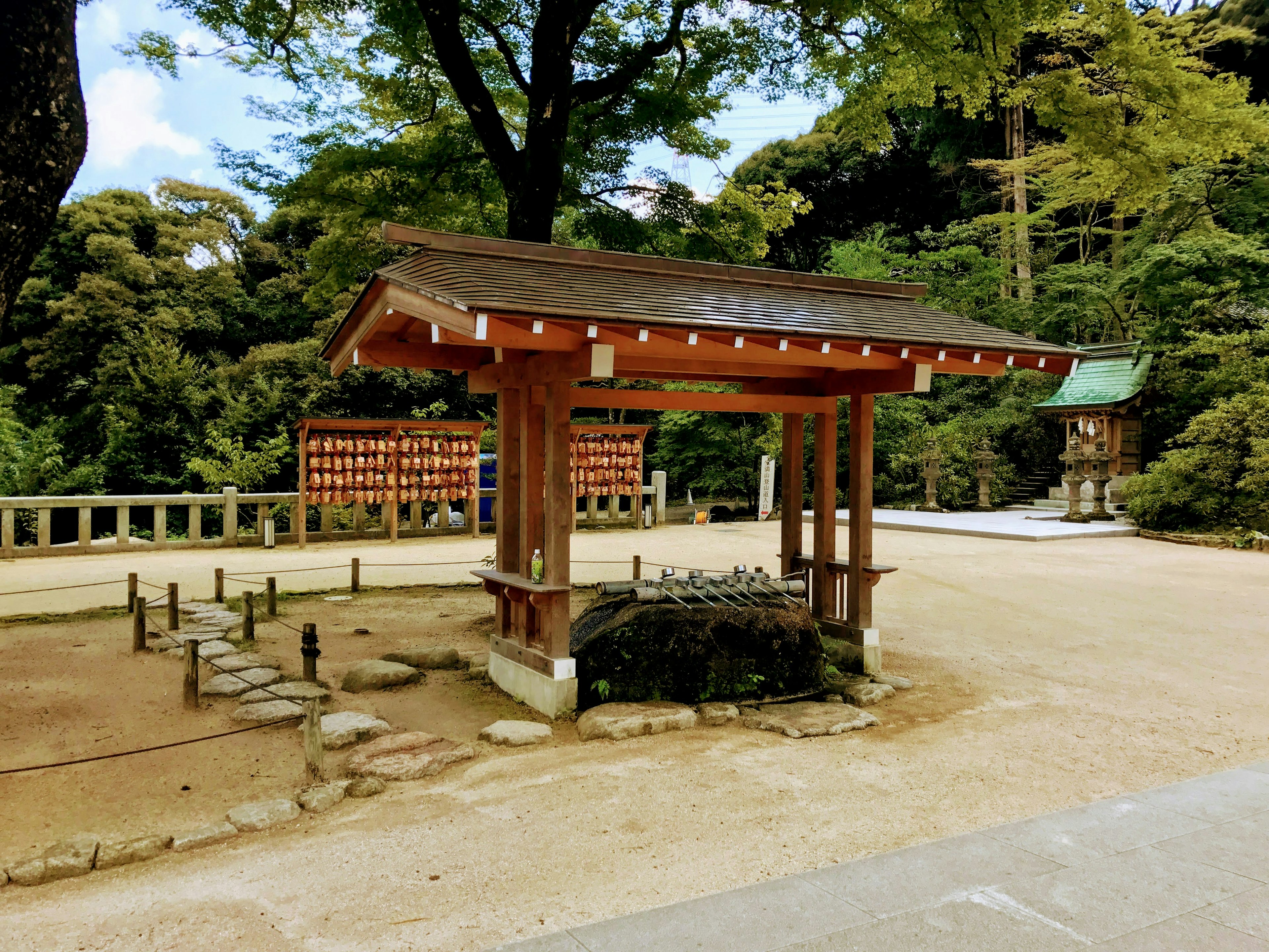 Traditional wooden structure in a serene park setting surrounded by lush trees and blue sky