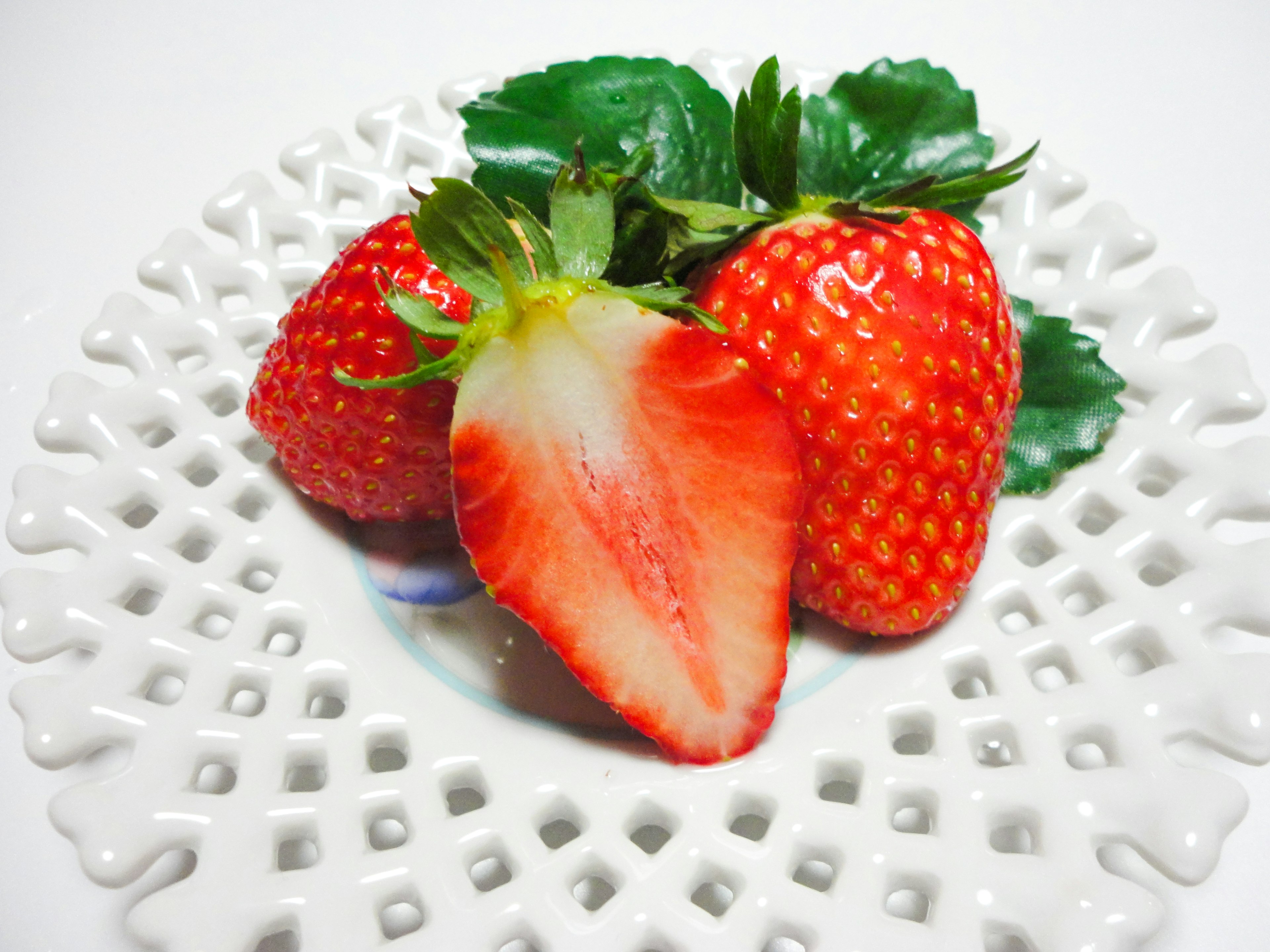 Fresh strawberries on a white plate with one cut in half