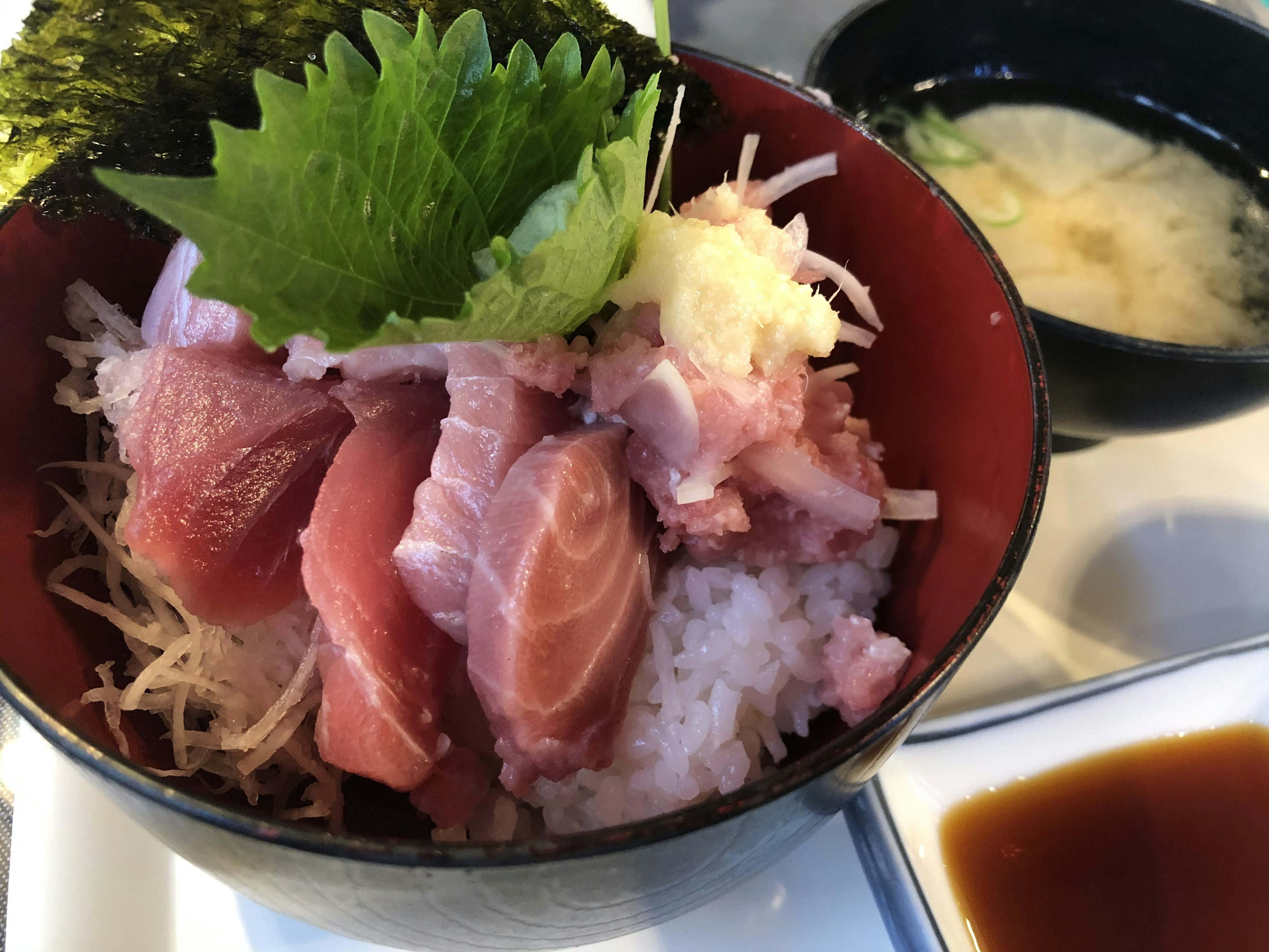 Image of a rice bowl topped with fresh sashimi and garnished with shiso leaves and ginger