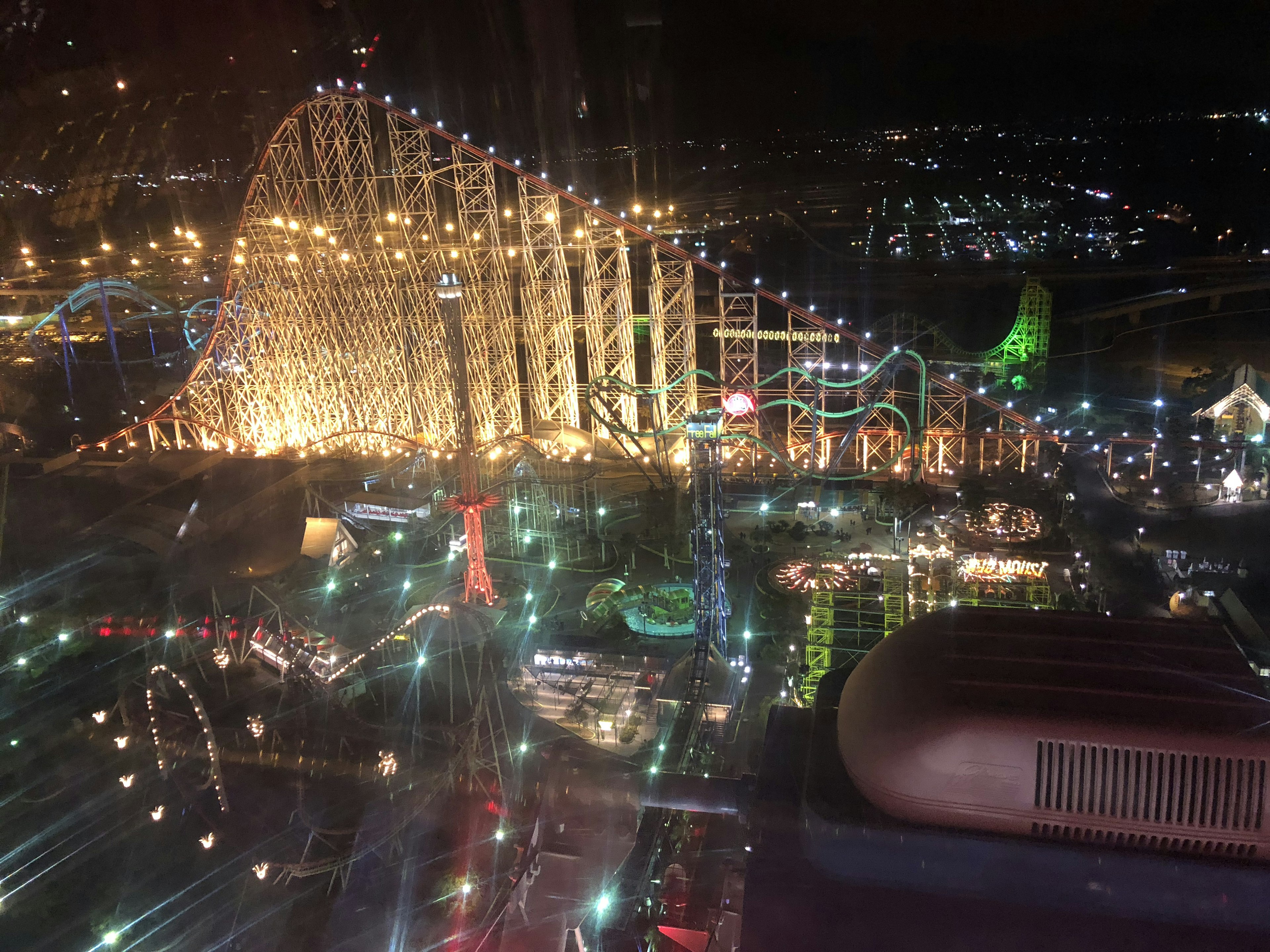 Parque de atracciones brillante con noria y montaña rusa de noche