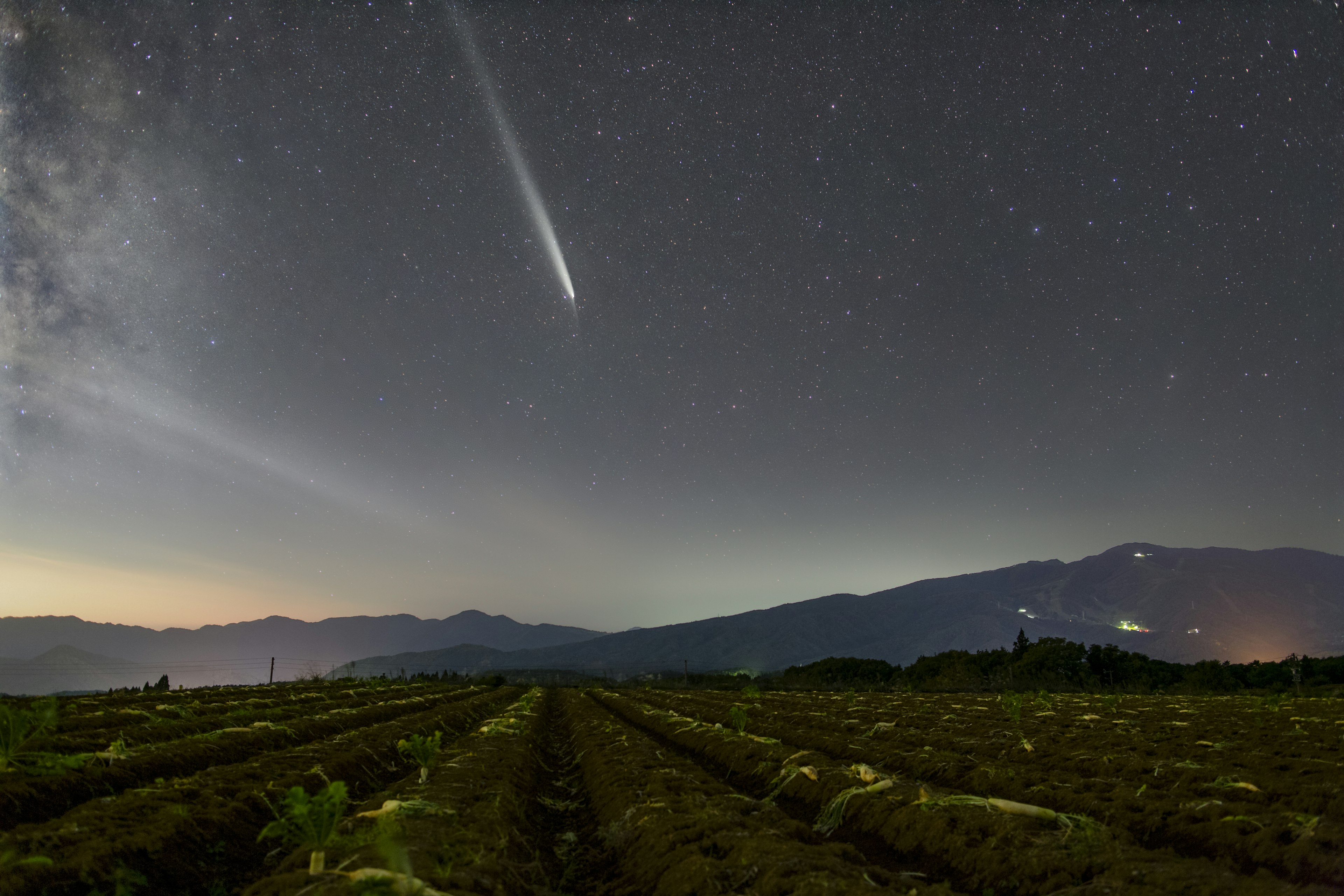 星空の下に広がる農場と流星のような彗星が見える風景