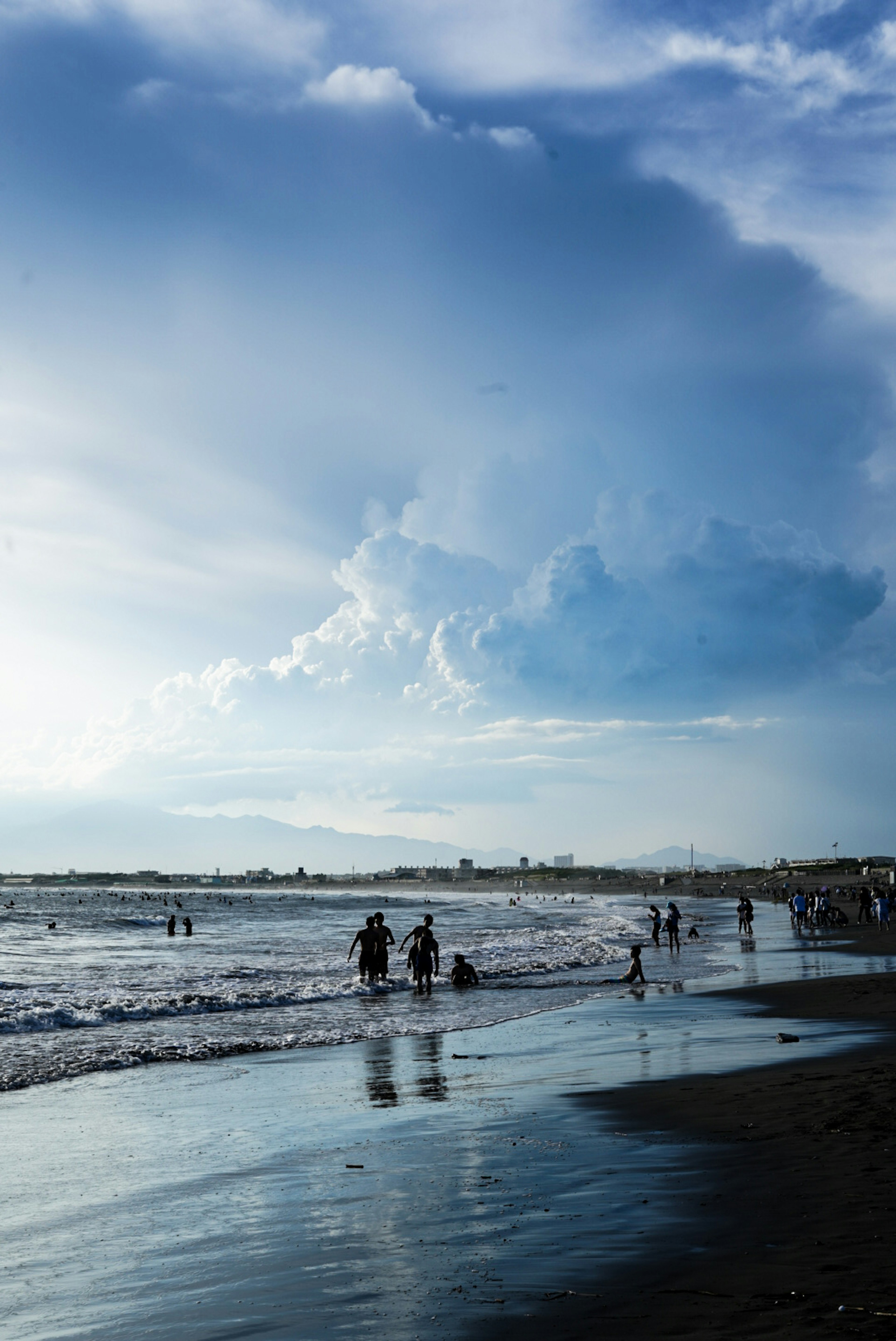 青い空と海に映る人々のシルエットが特徴的なビーチの風景