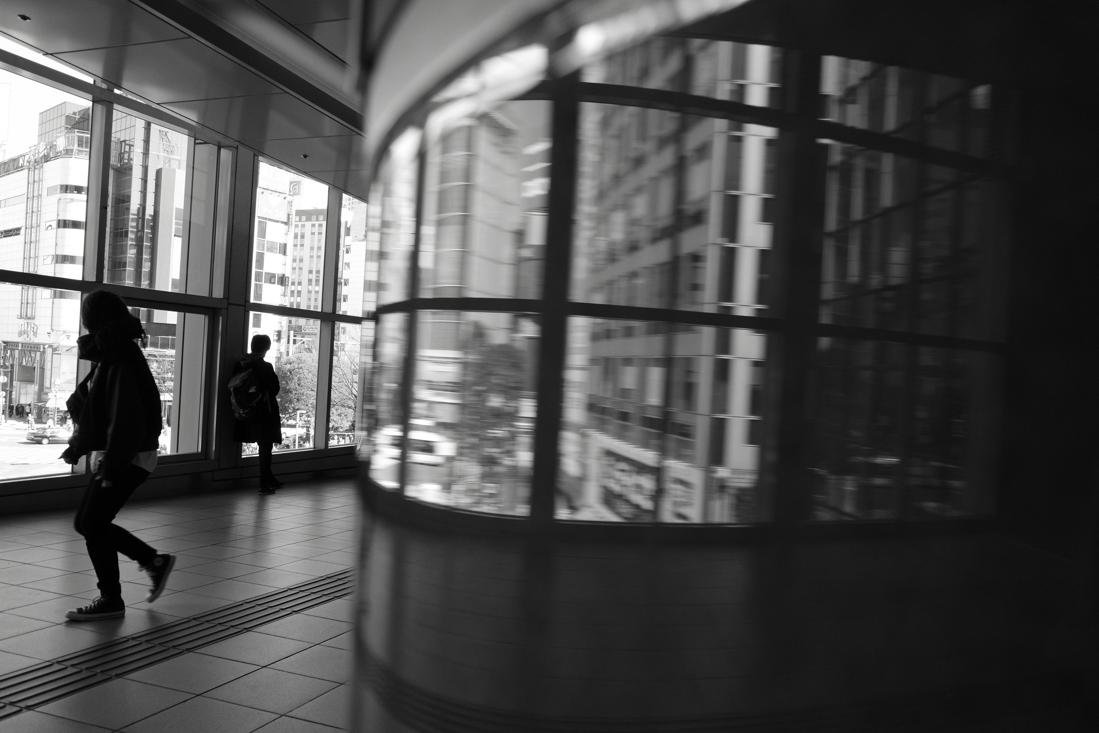 Escena urbana en blanco y negro con reflejos en una pared de vidrio y siluetas de personas