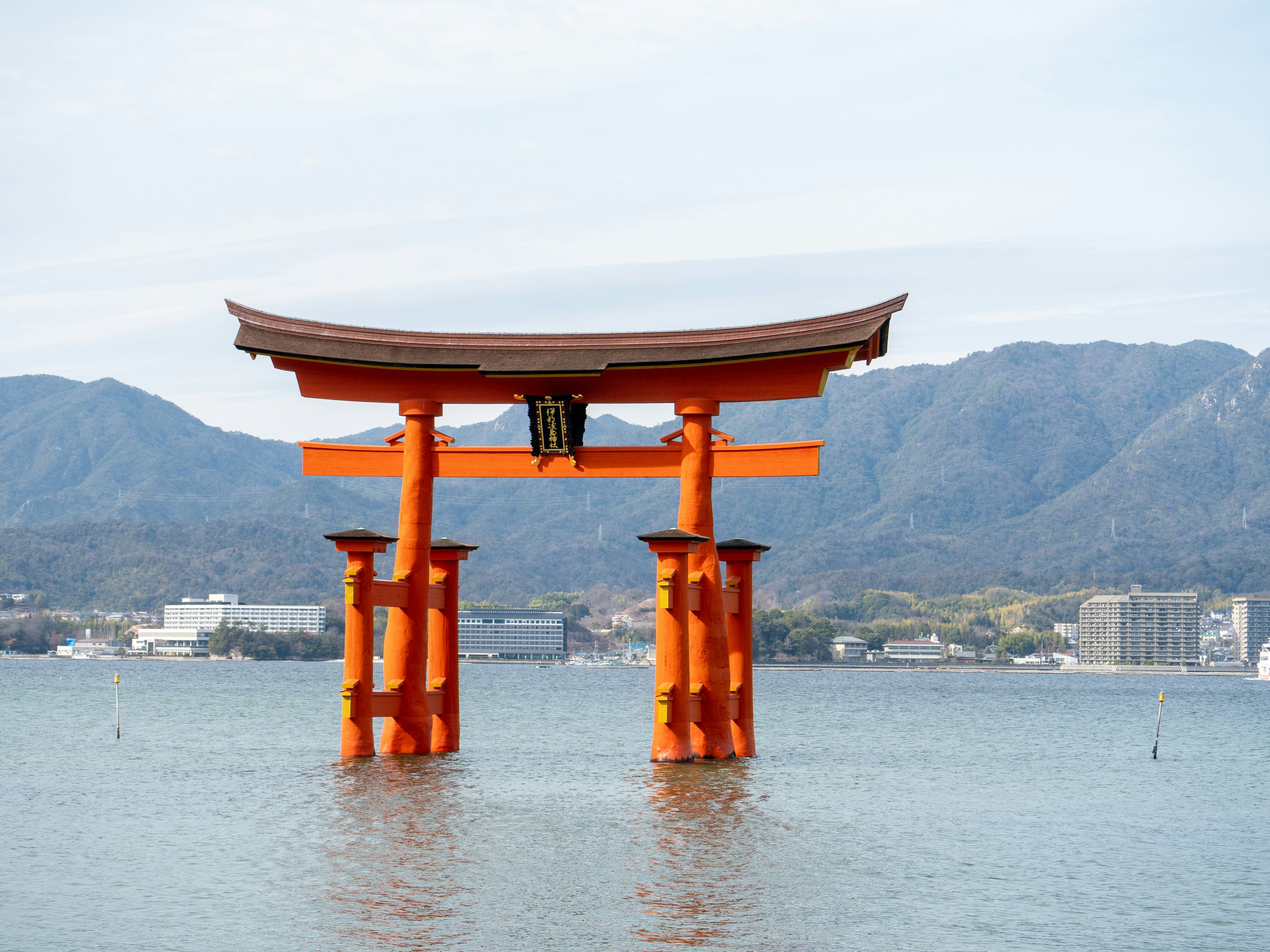 Cổng torii đỏ nổi trên biển với núi ở phía sau